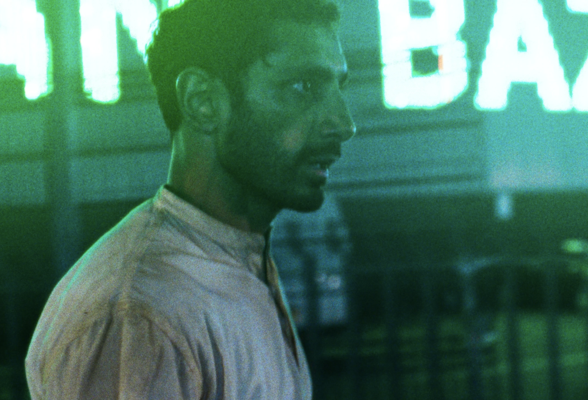 A man of Pakistani descent, in his thirties, walks through neon-lit streets, looking worse for wear.