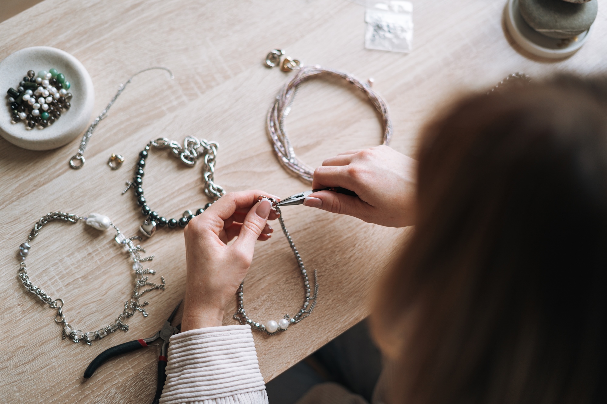 Young woman jewelry designer creating necklace and working at table in the studio.
