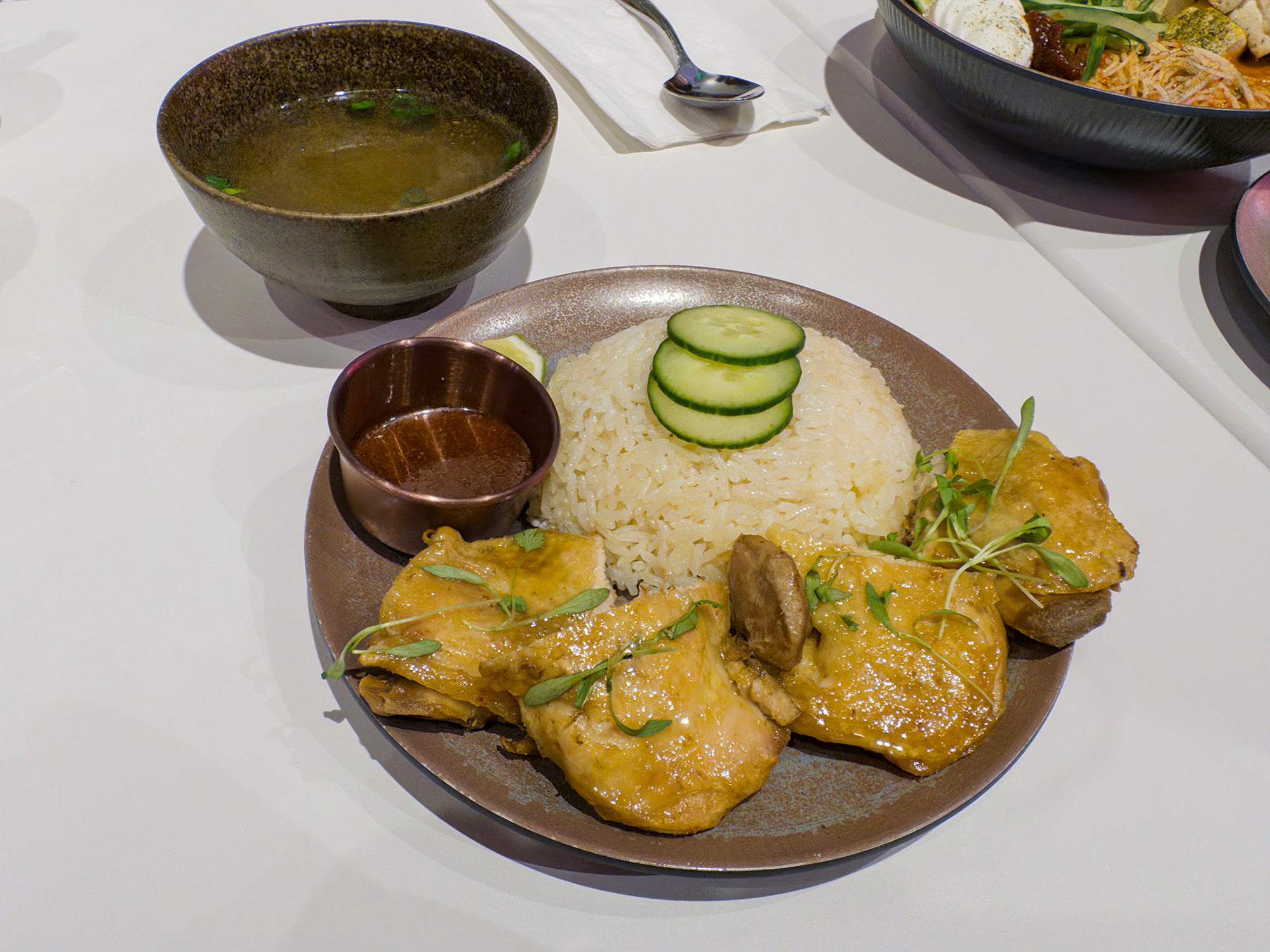 Plate of Hainan-style chicken rice, with a bowl of broth on the side.