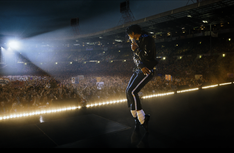 An actor playing Michael Jackson recreates Jackson's signature toe-point dance move on an stadium stage.