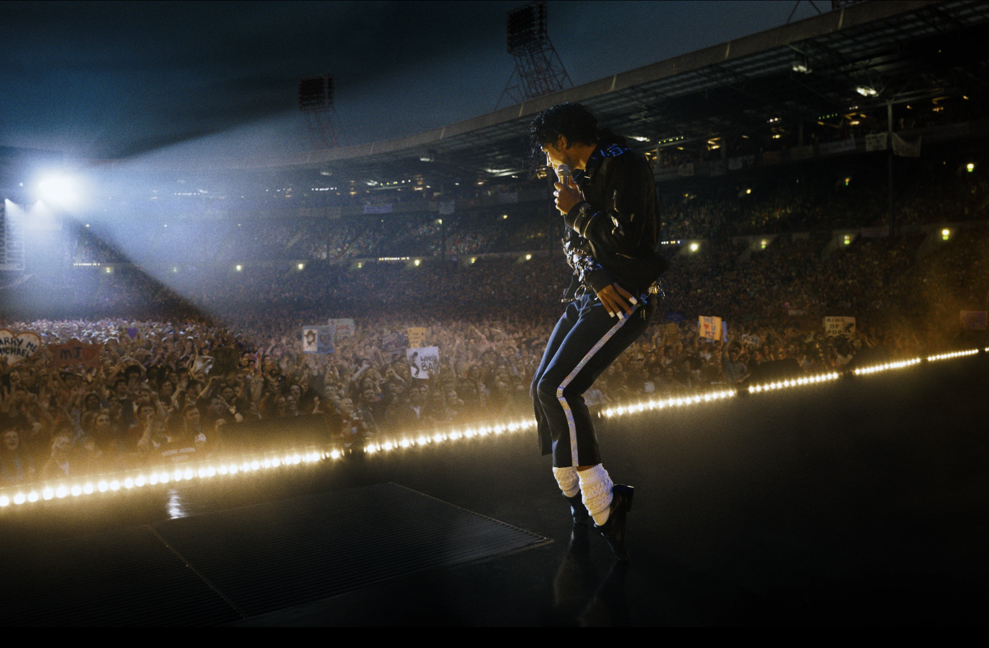 An actor playing Michael Jackson recreates Jackson's signature toe-point dance move on an stadium stage.
