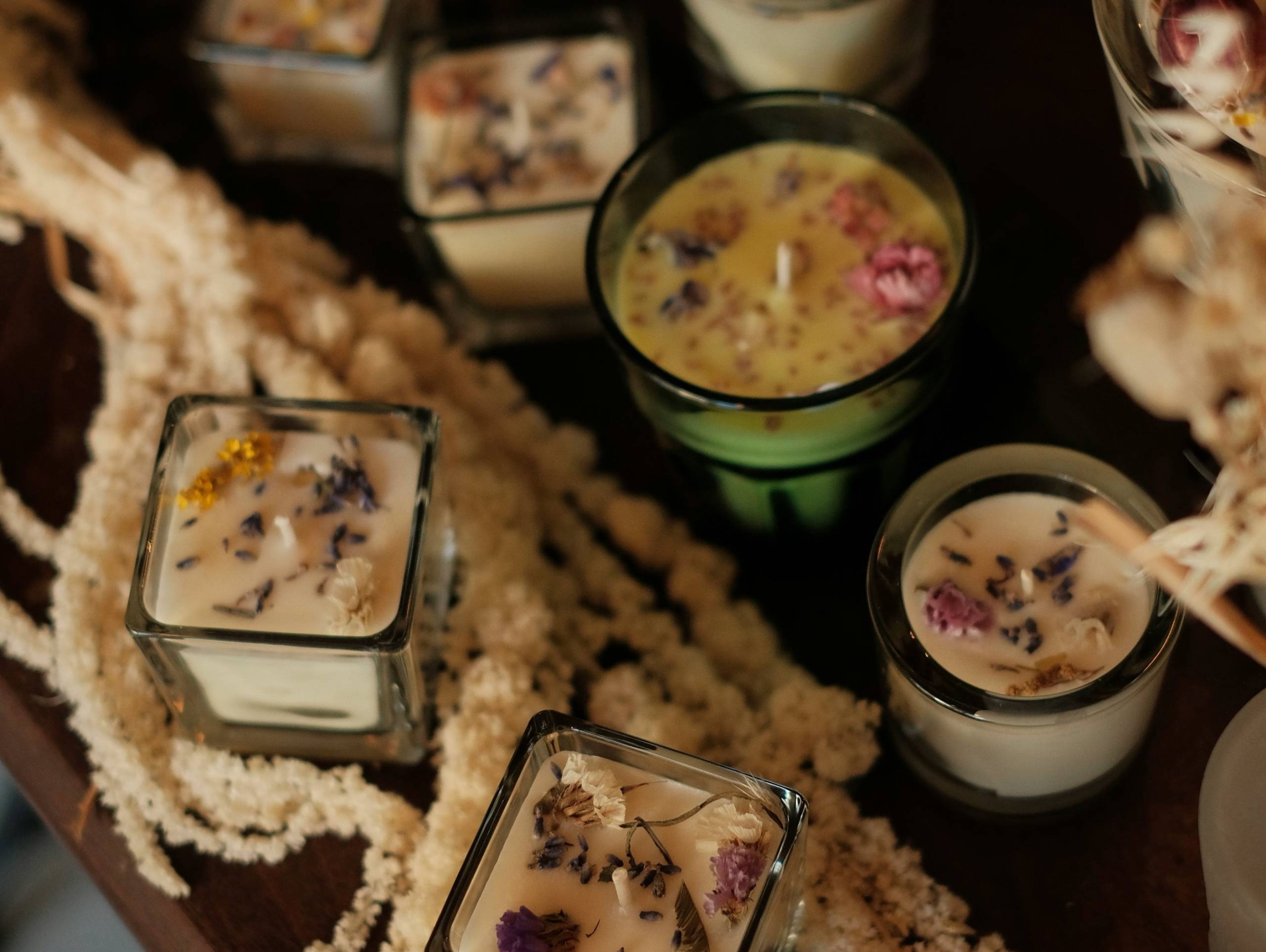 A selection of small candles in various glass receptacles, complete with herbs and petals.