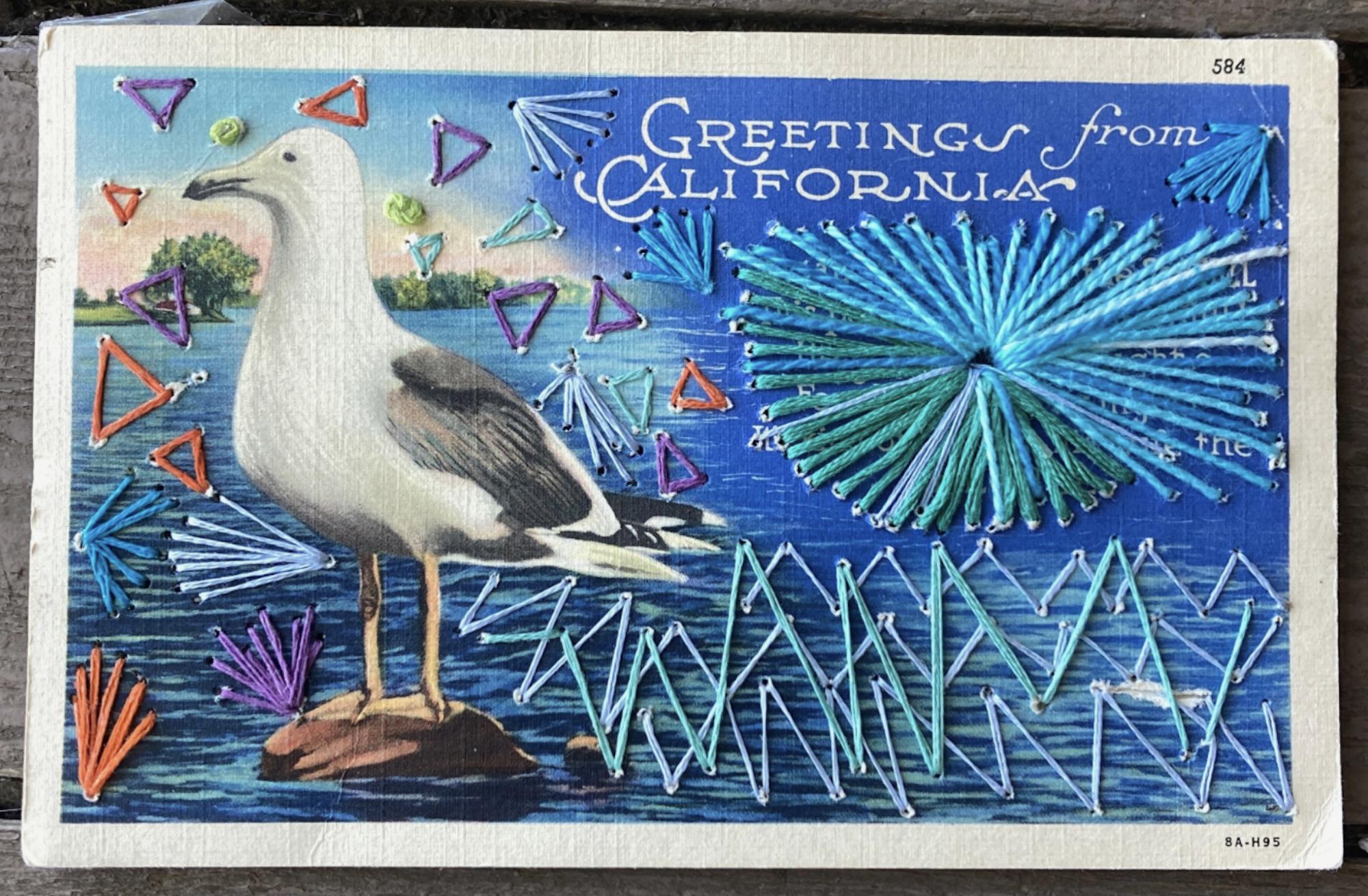 A postcard featuring a seagull and the words 'Greetings from California' that's been enhanced by embroidery stitching.