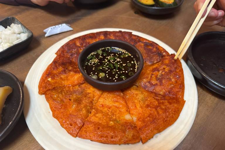A very crispy-looking, orange-tinted kimchi pancake, cut in wedges on a plate.