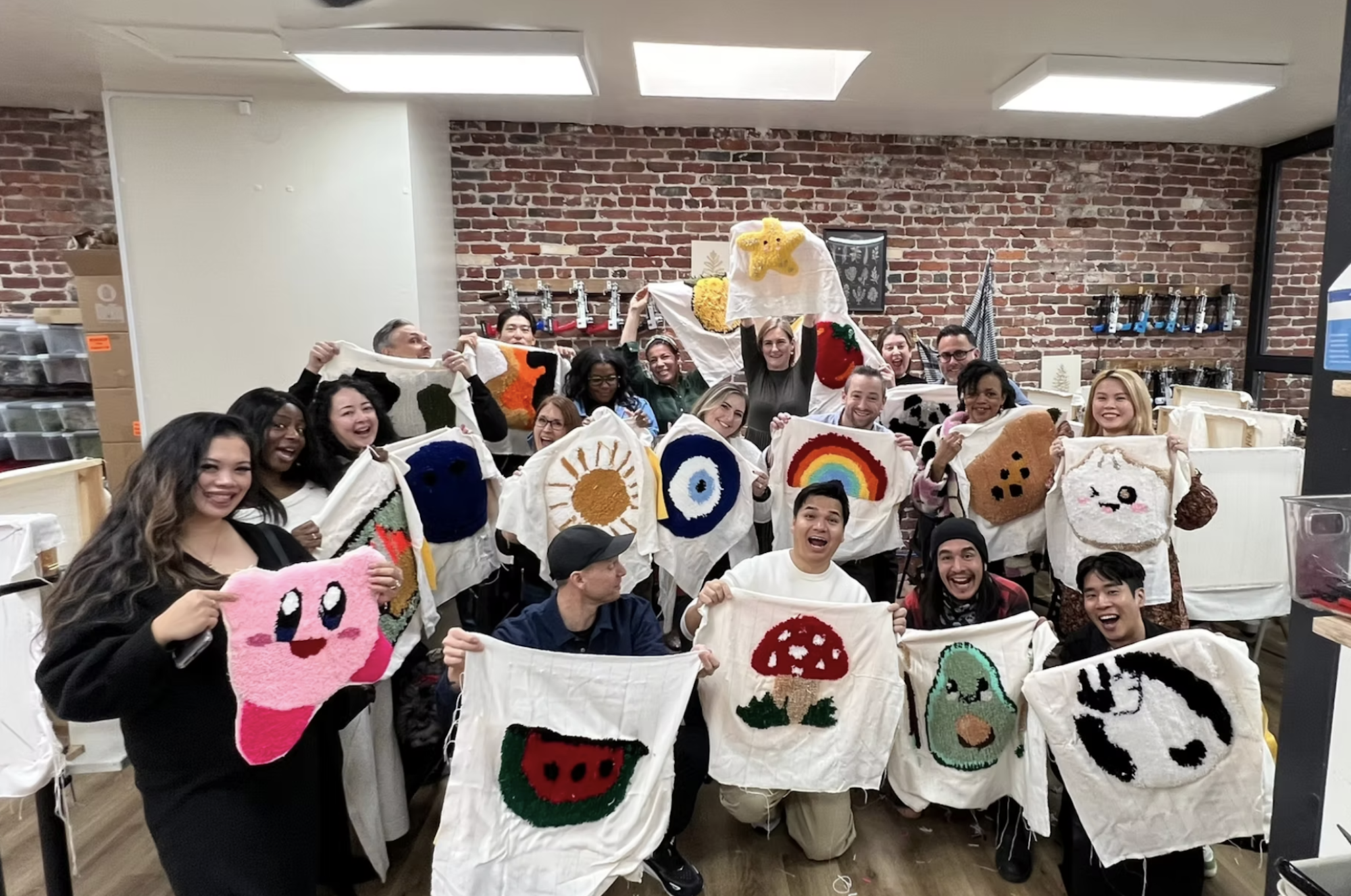 A group of students in a classroom smile and hold up art projects made from tufted fabric.