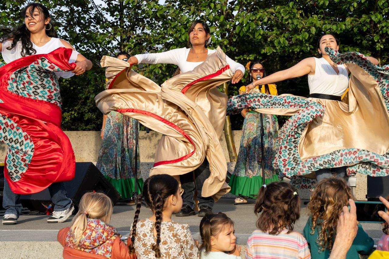 A trio of young women dance on stage, while a handful of children watch from the front row. 