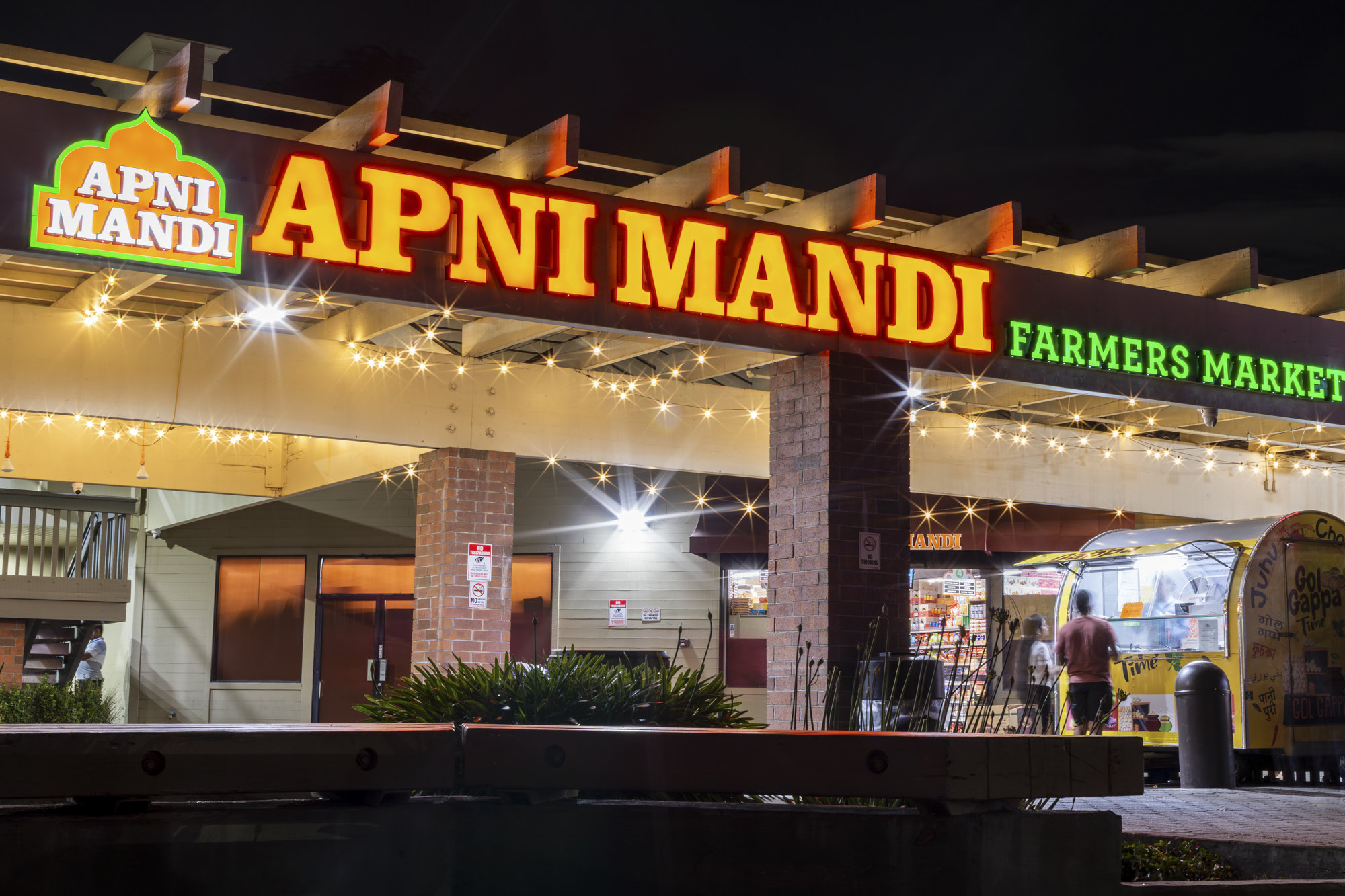An Indian supermarket lit up at night. The sign above reads, "Apni Mandi."