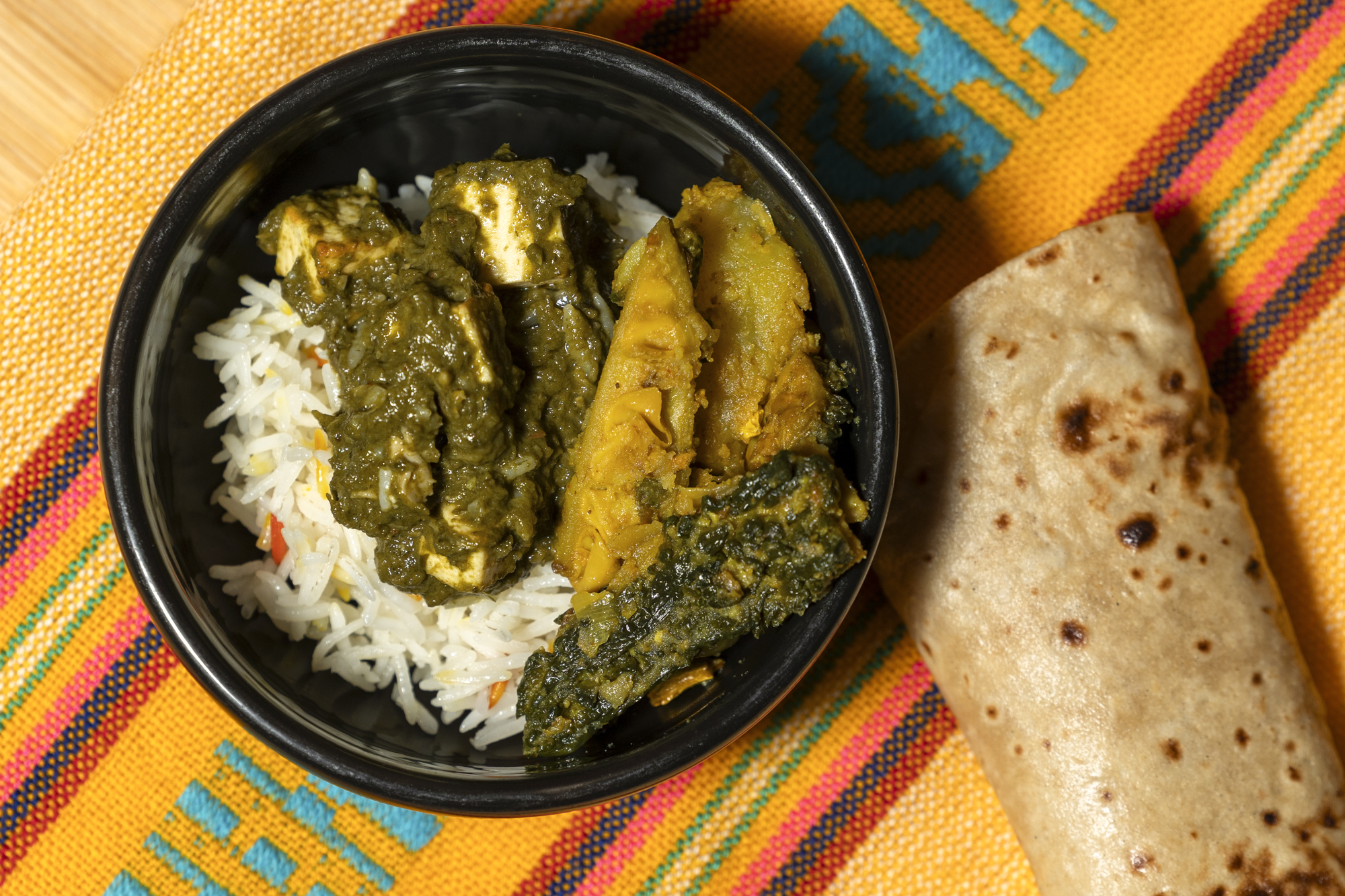 Takeout container with basmati rice and two kinds of curry, on a colorful tablecloth.