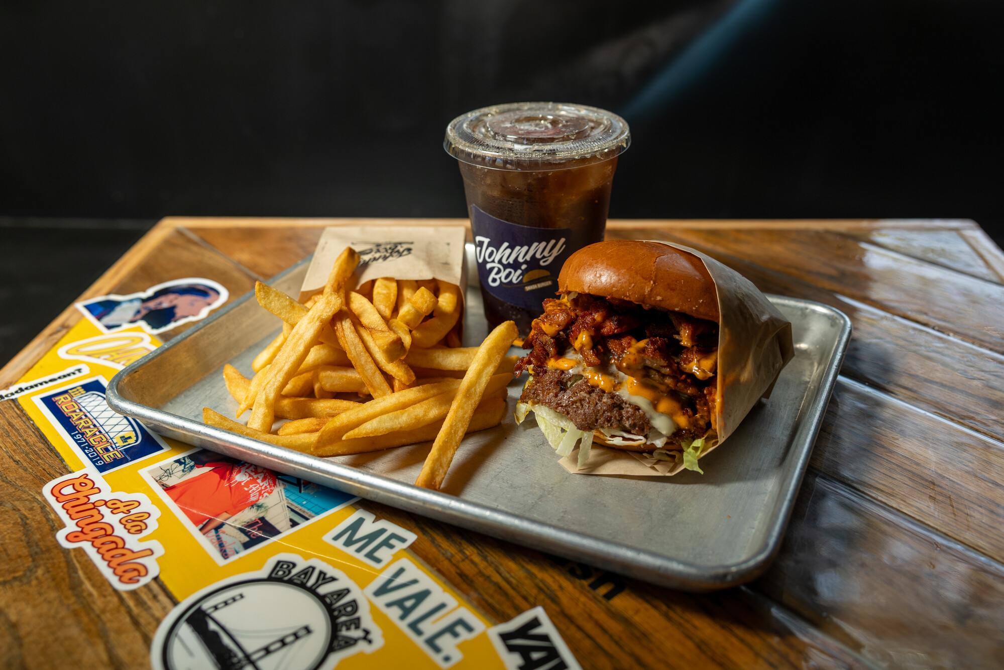 An overstuffed burger, fries and soda on a metal try.