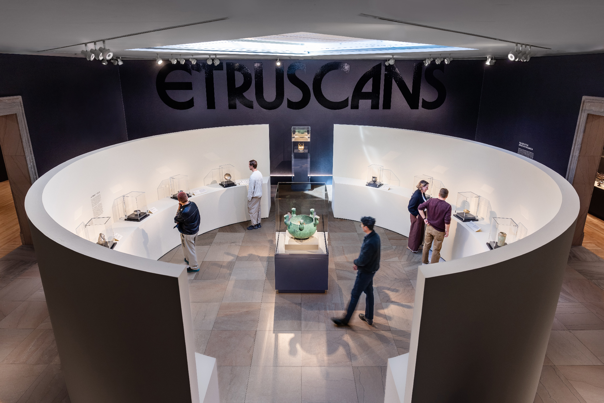 curved display with objects in vitrines, show title in black on wall