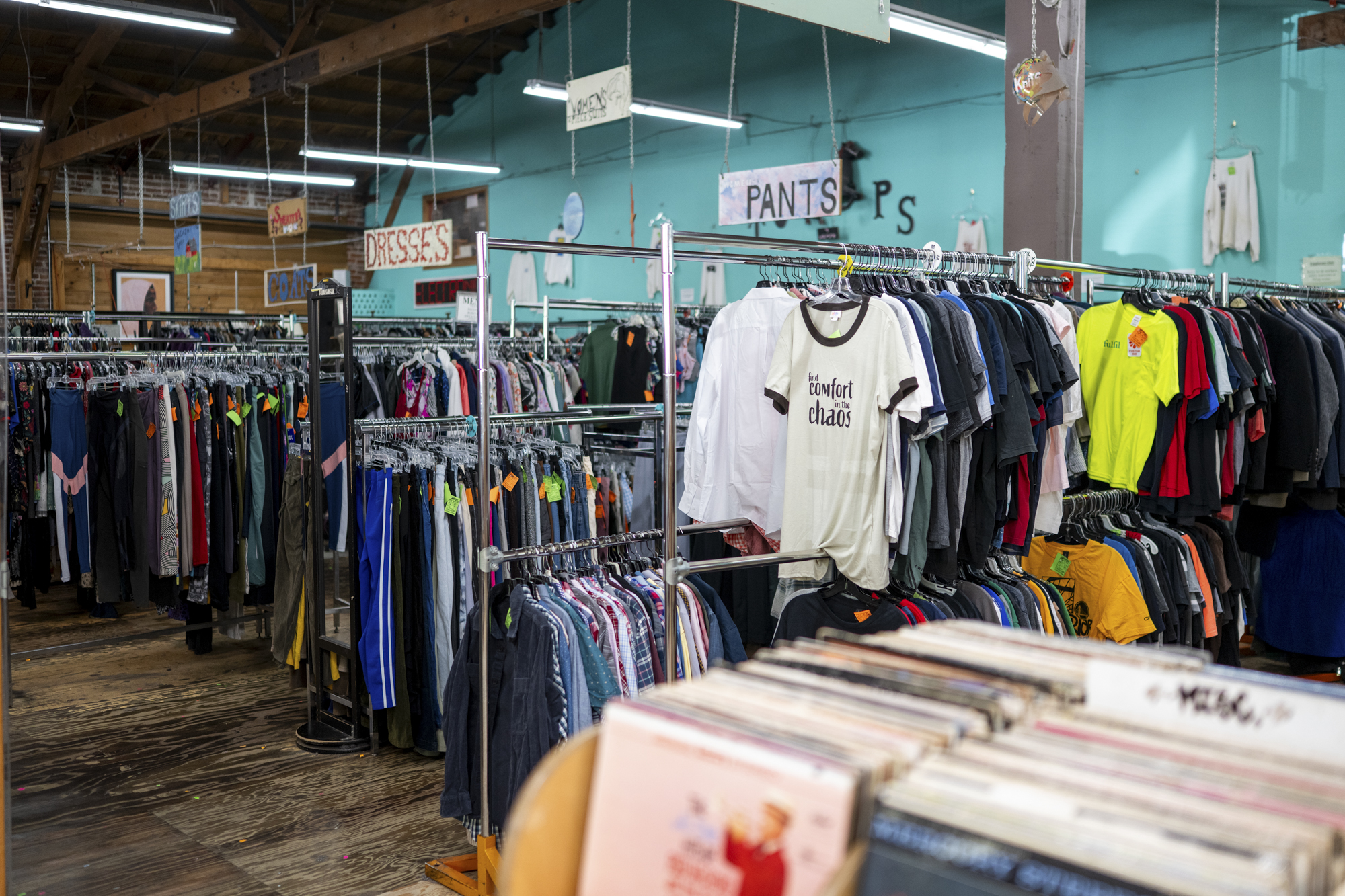 Racks of T-shirts are lined up against a baby blue wall as vinyl LPs are stacked in the foreground