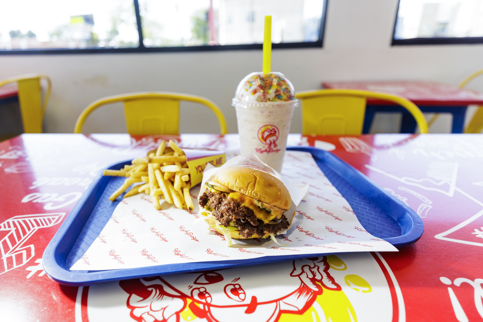 Burger, fries and a colorful, Fruity Pebbles-topped milkshake on a tray.