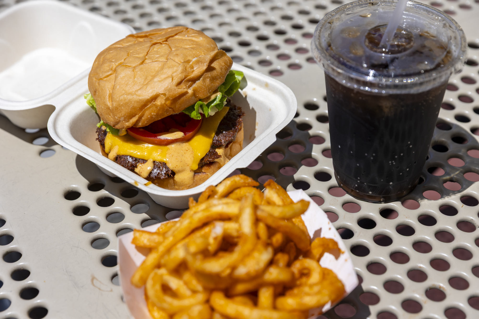 A cheeseburger, fries and cola on a metal picnic table.