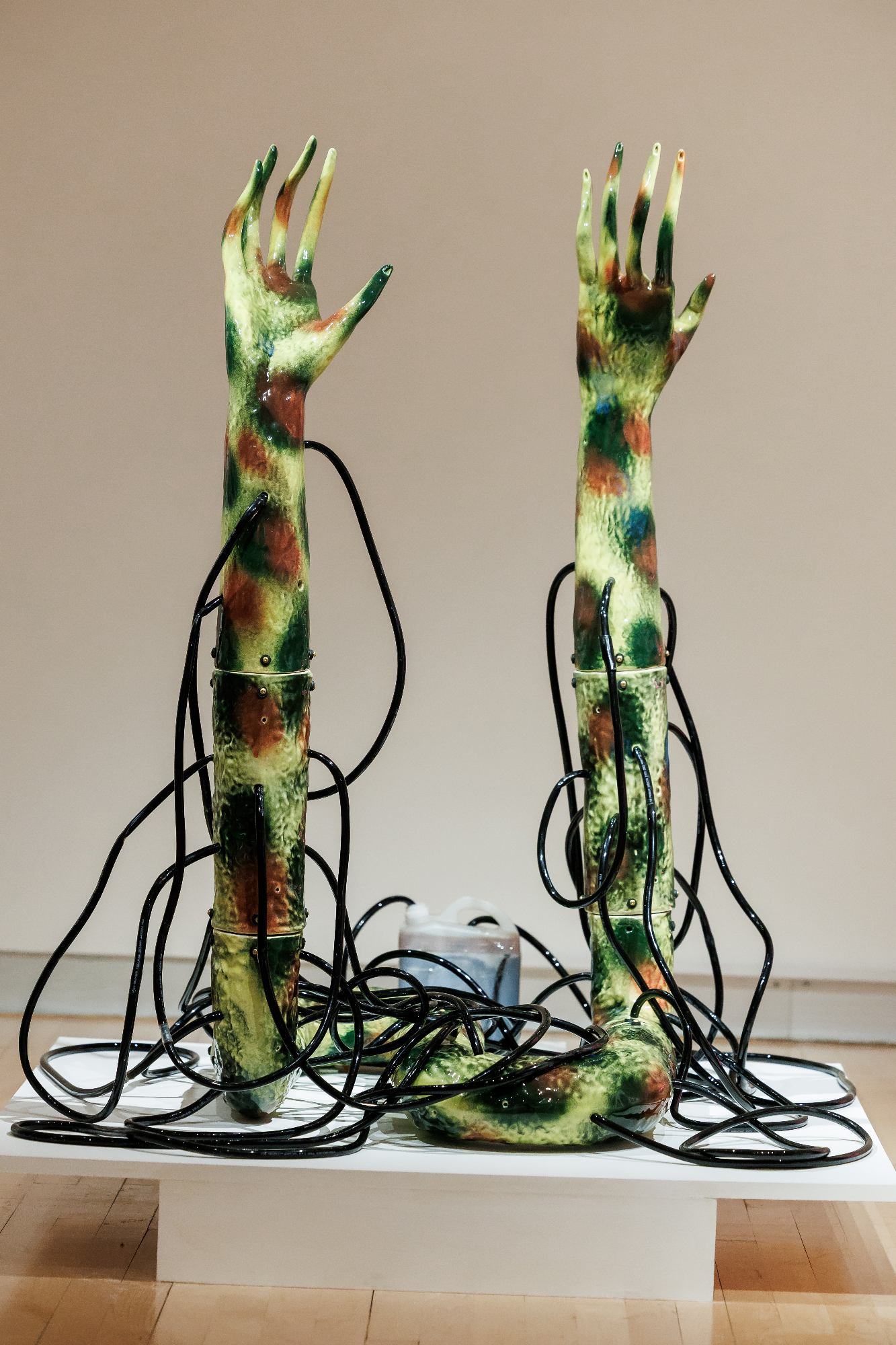 ceramic sculpture of green-spotted hands with black tubing tangled around