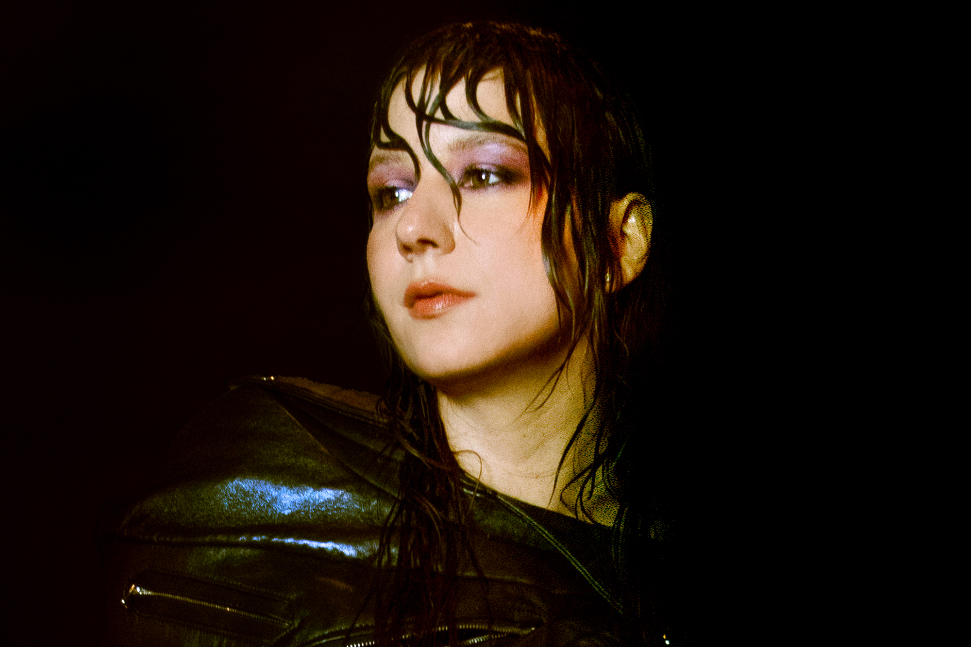 person looks dramatically over their right shoulder against dark background