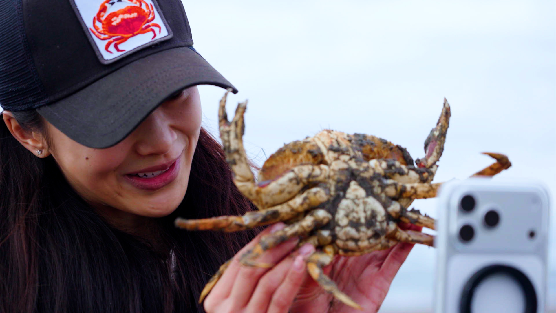 person in hat holds crab in front of phone camera