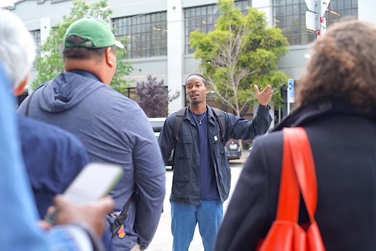 A man standing outside, addressing a crowd of people.
