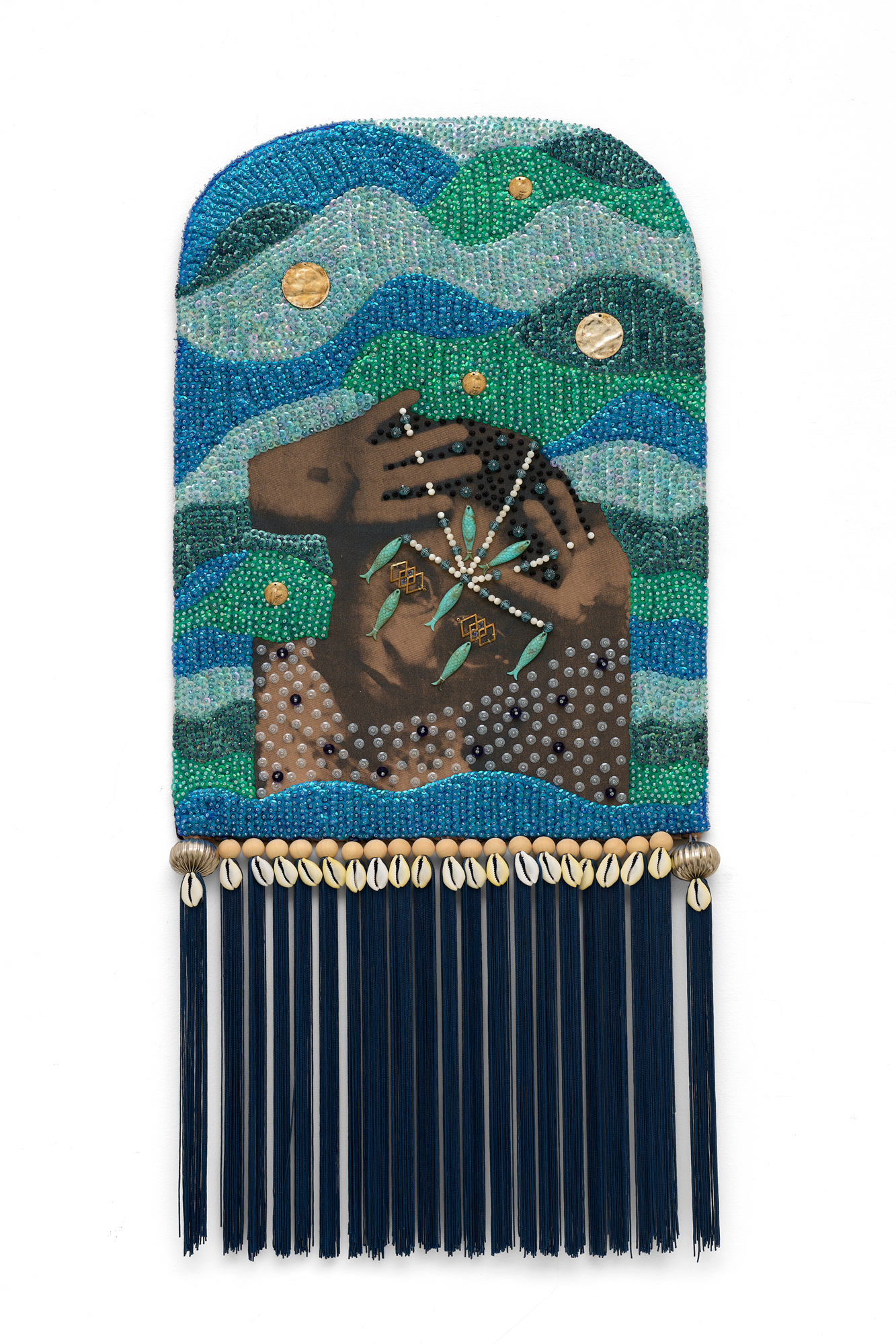 beaded artwork of person with hands at head, densely covered in shells and tassels
