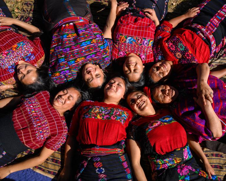 group of women laying down with heads together, wearing embroidered colorful shirts