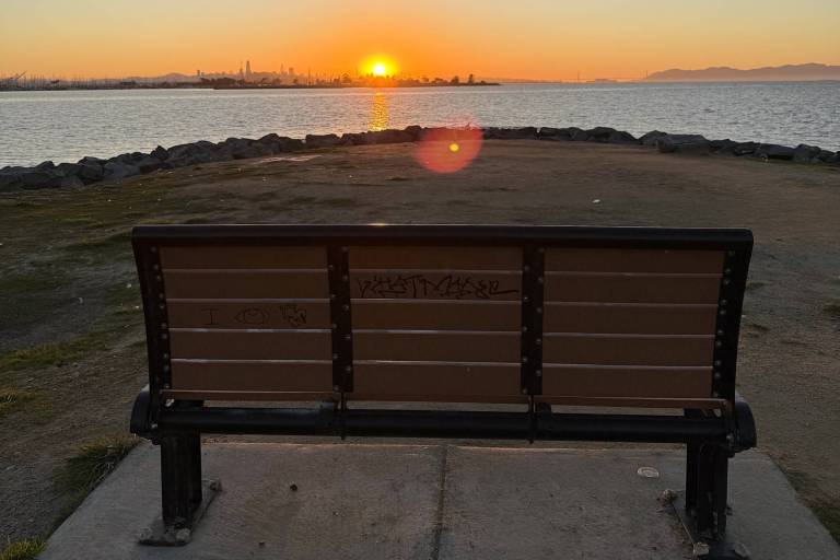 A bench in the foreground with the sun setting into the bay behind it.
