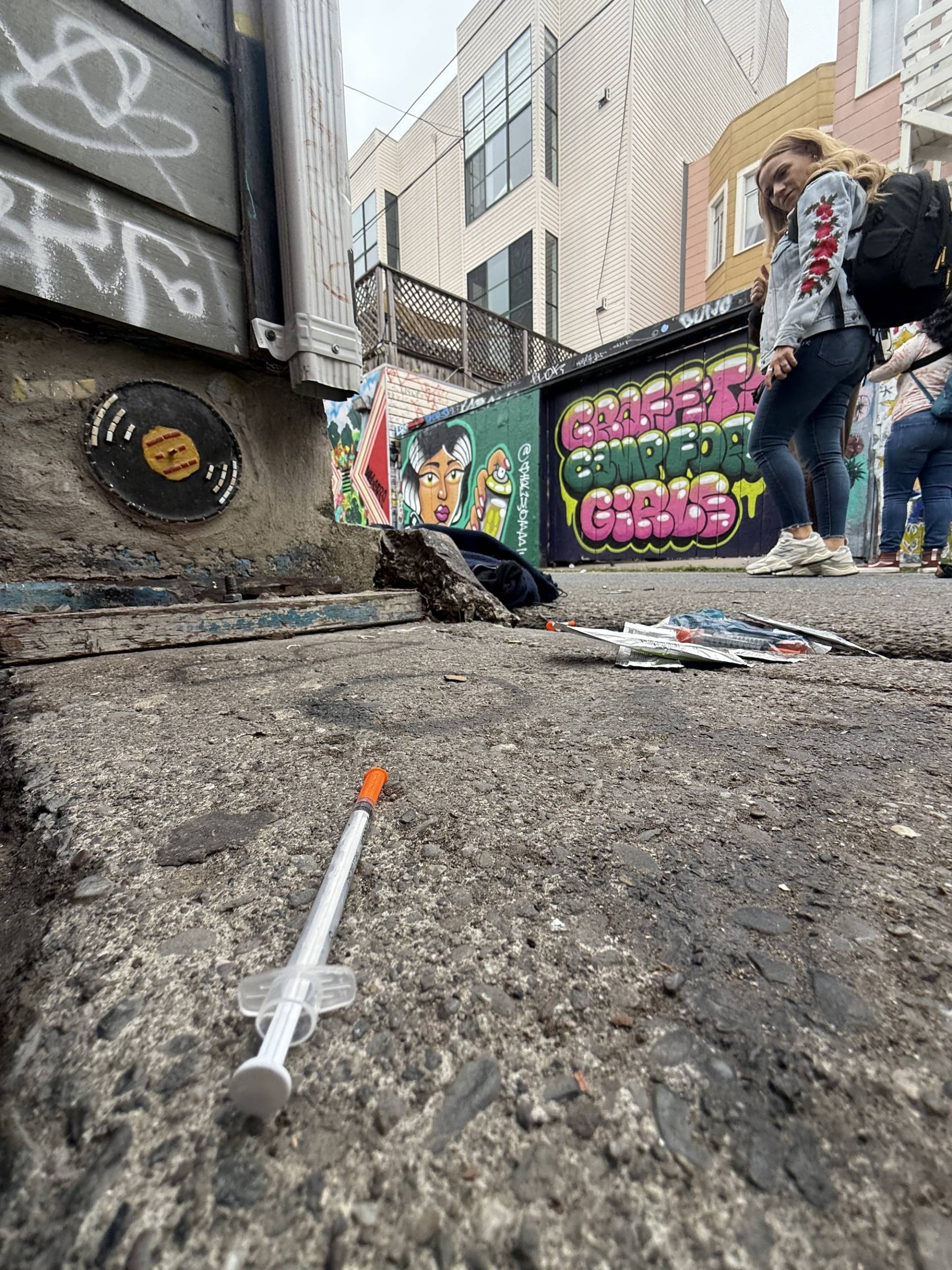 A woman walks past and looks down at a hypodermic needle on the ground in San Francisco. 