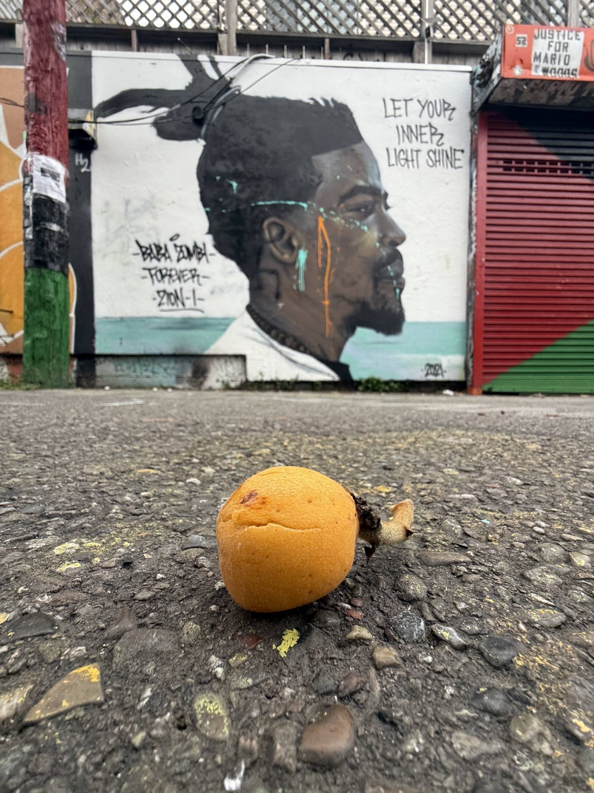 A fallen piece of fruit sits in font of a colorfully painted portrait image of an African American man.