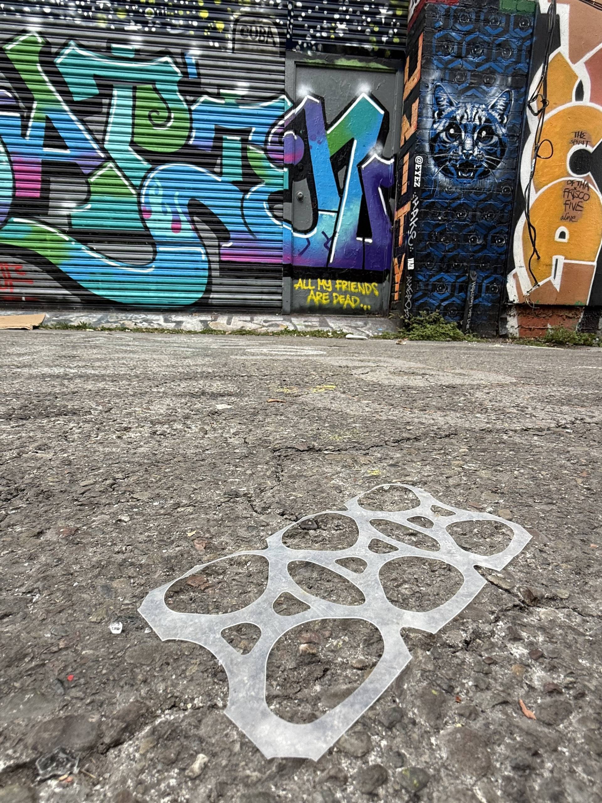 Translucent 6-pack plastic rings sit in front of a mural in an alleyway. 
