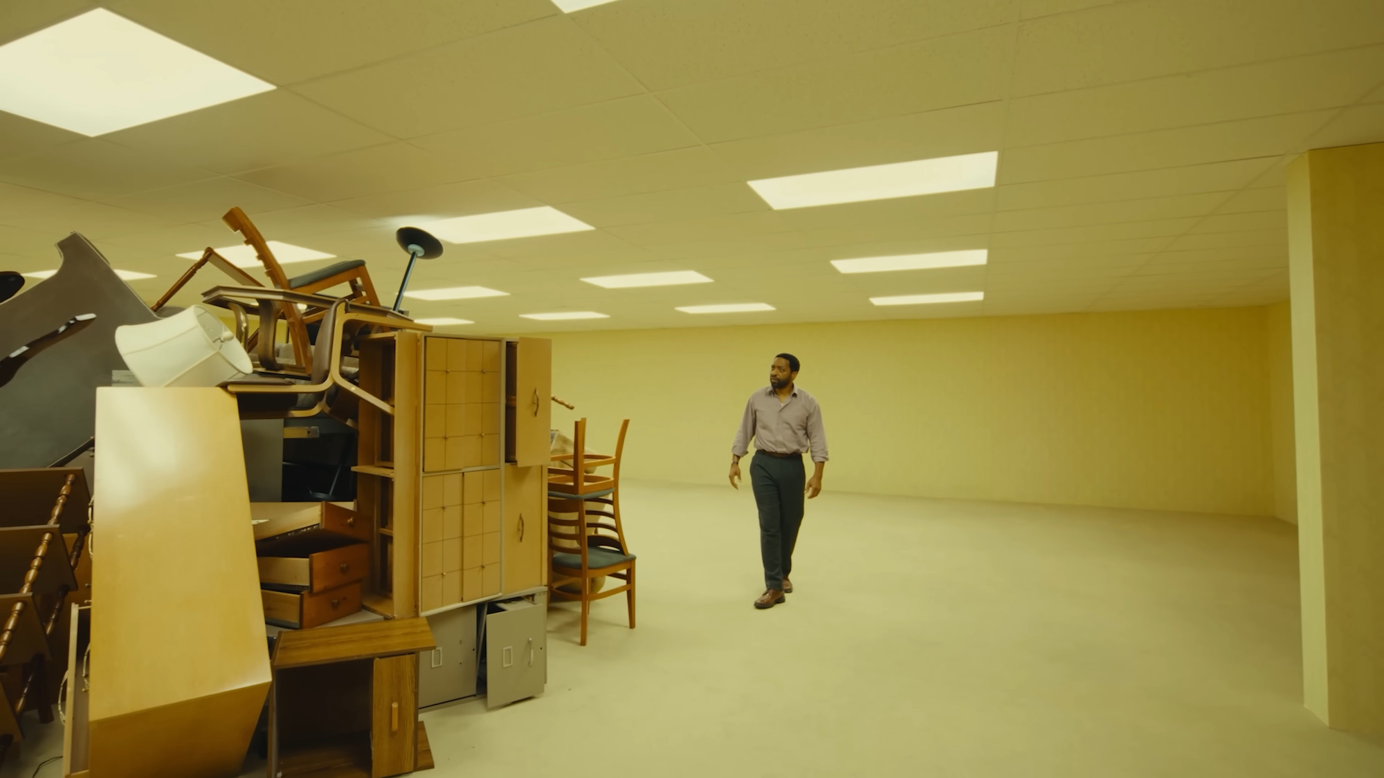 A Black man stands beside a pile of office furniture.