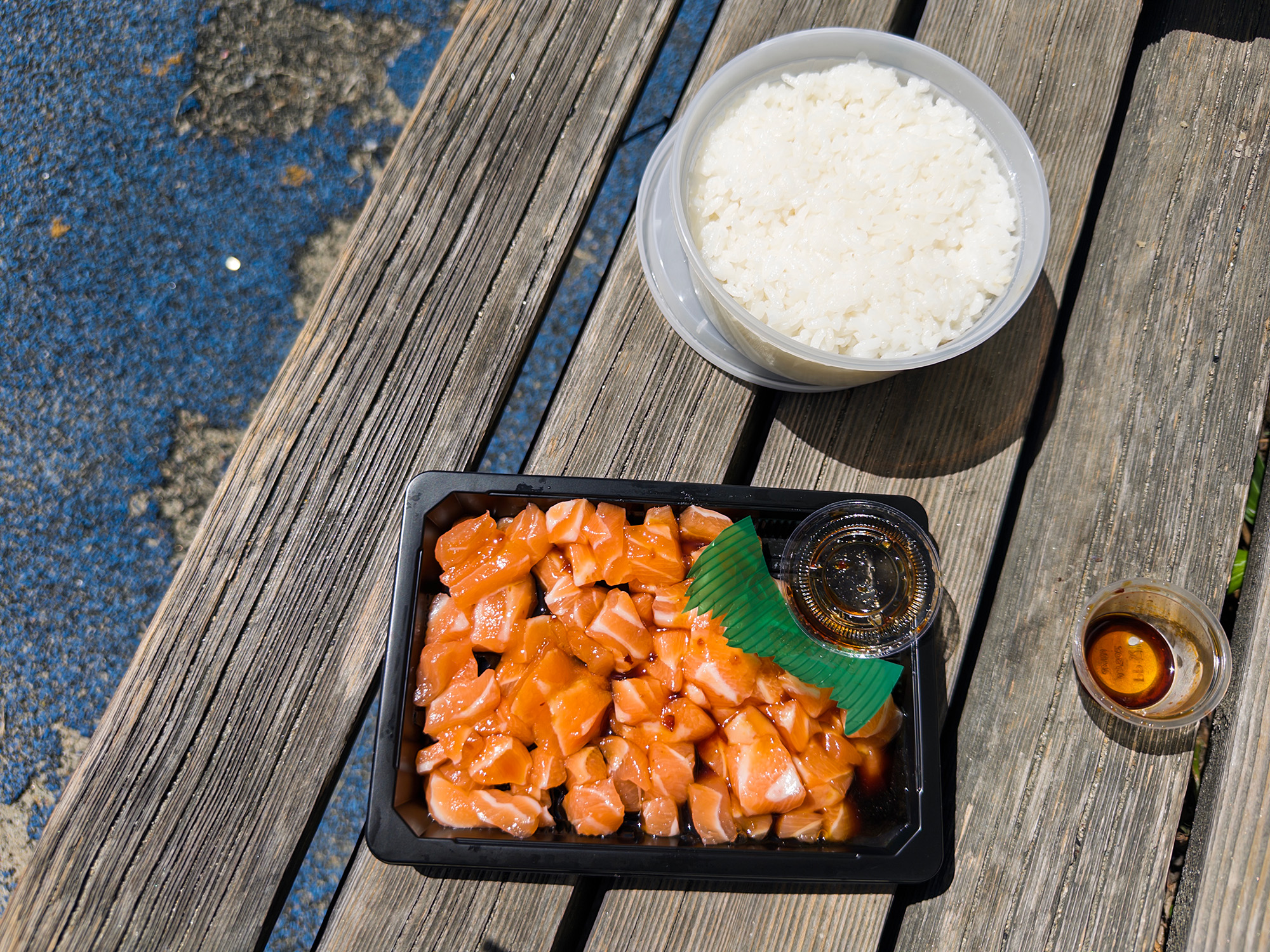 A container of salmon poke and a side of white rice, shown on a park bench.