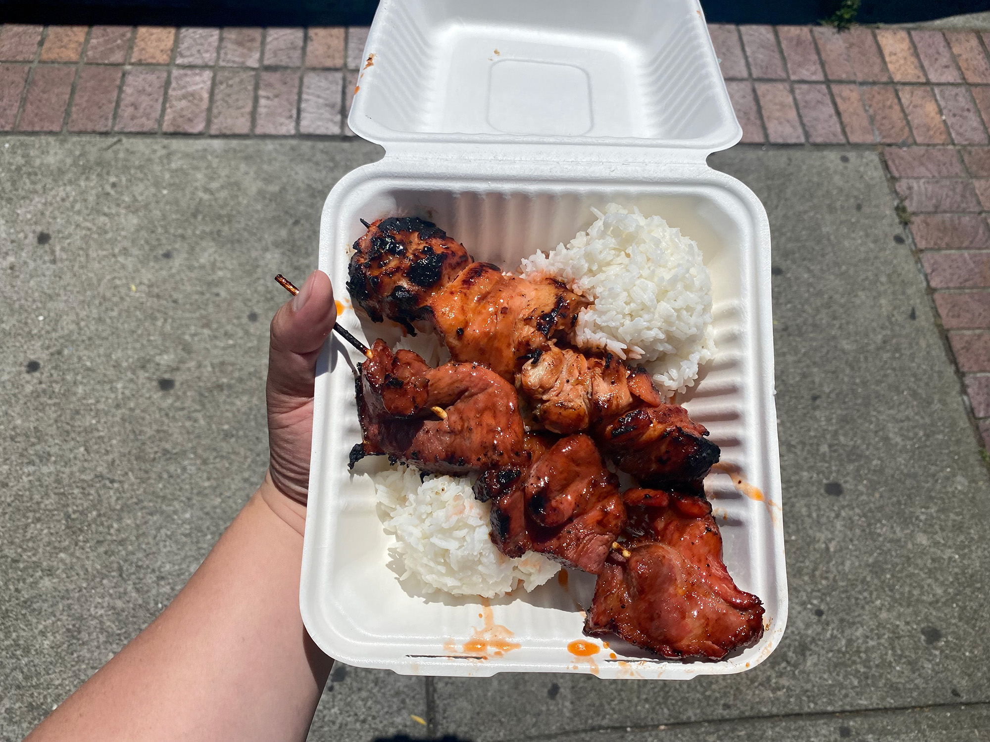 To-go container of barbecue skewers over white rice.