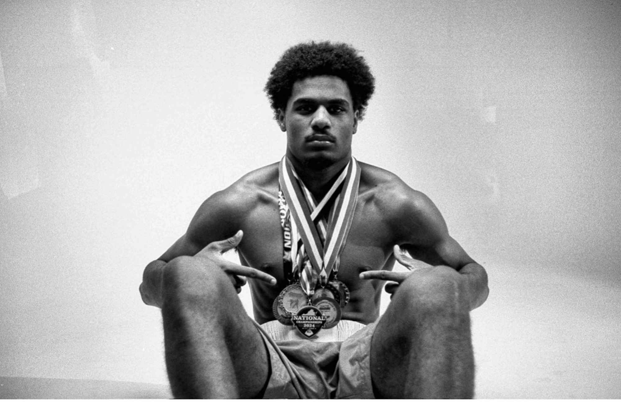 A black and white image of a young African American man wearing multiple medals around his neck. 