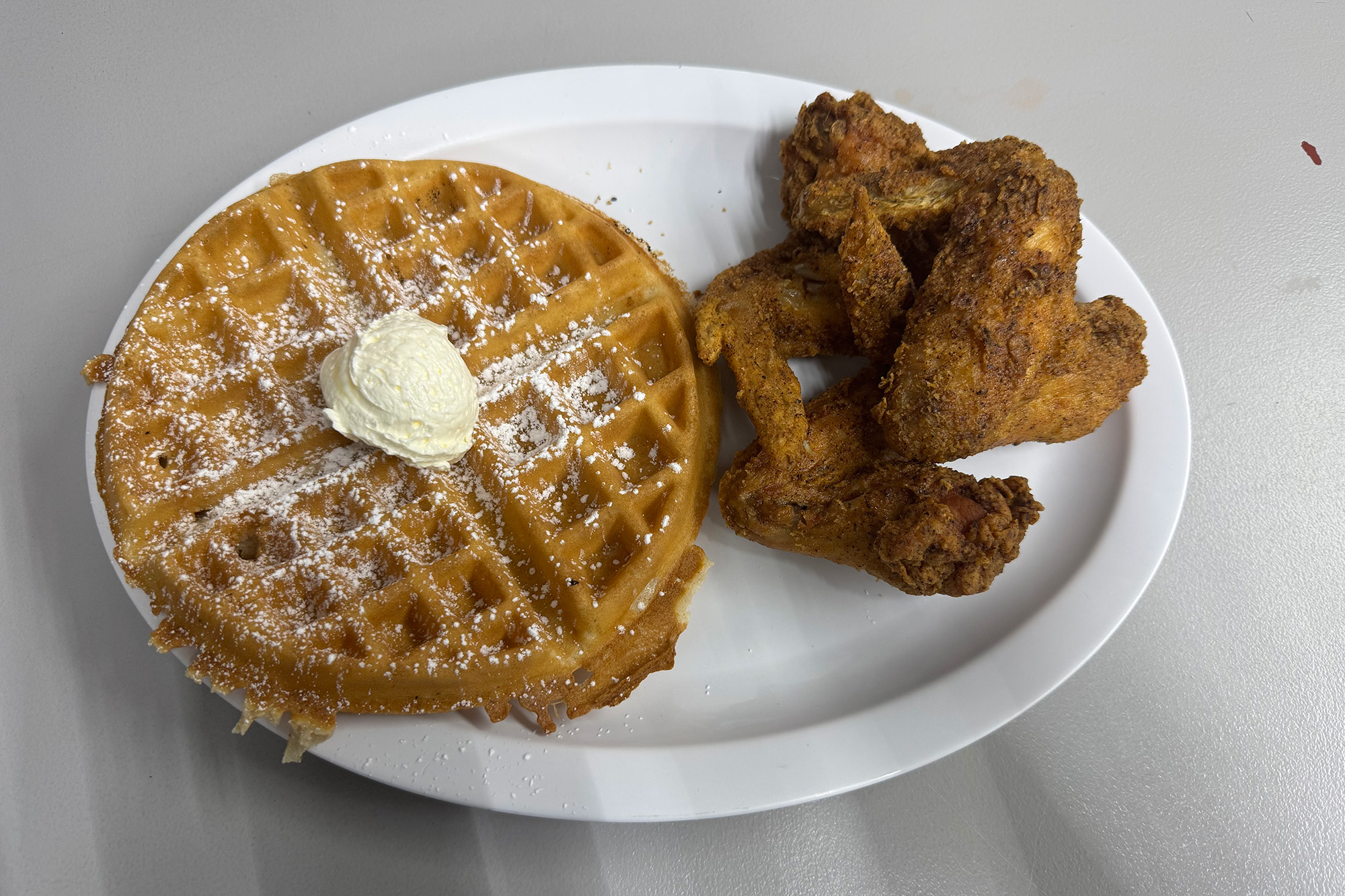A waffle and three chicken wings on a paper plate.
