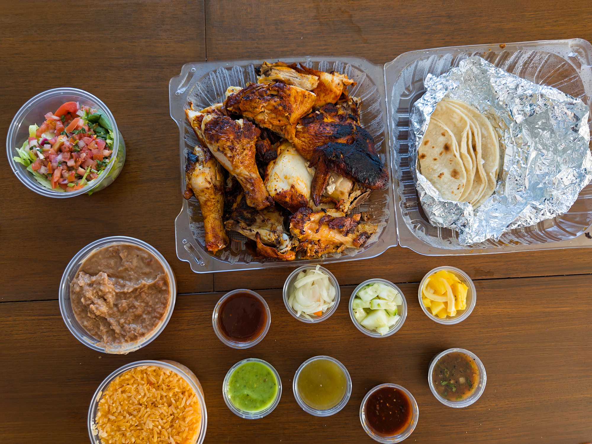 Whole grilled chicken in a takeout container, with rice, refried beans and various salsas on the side.