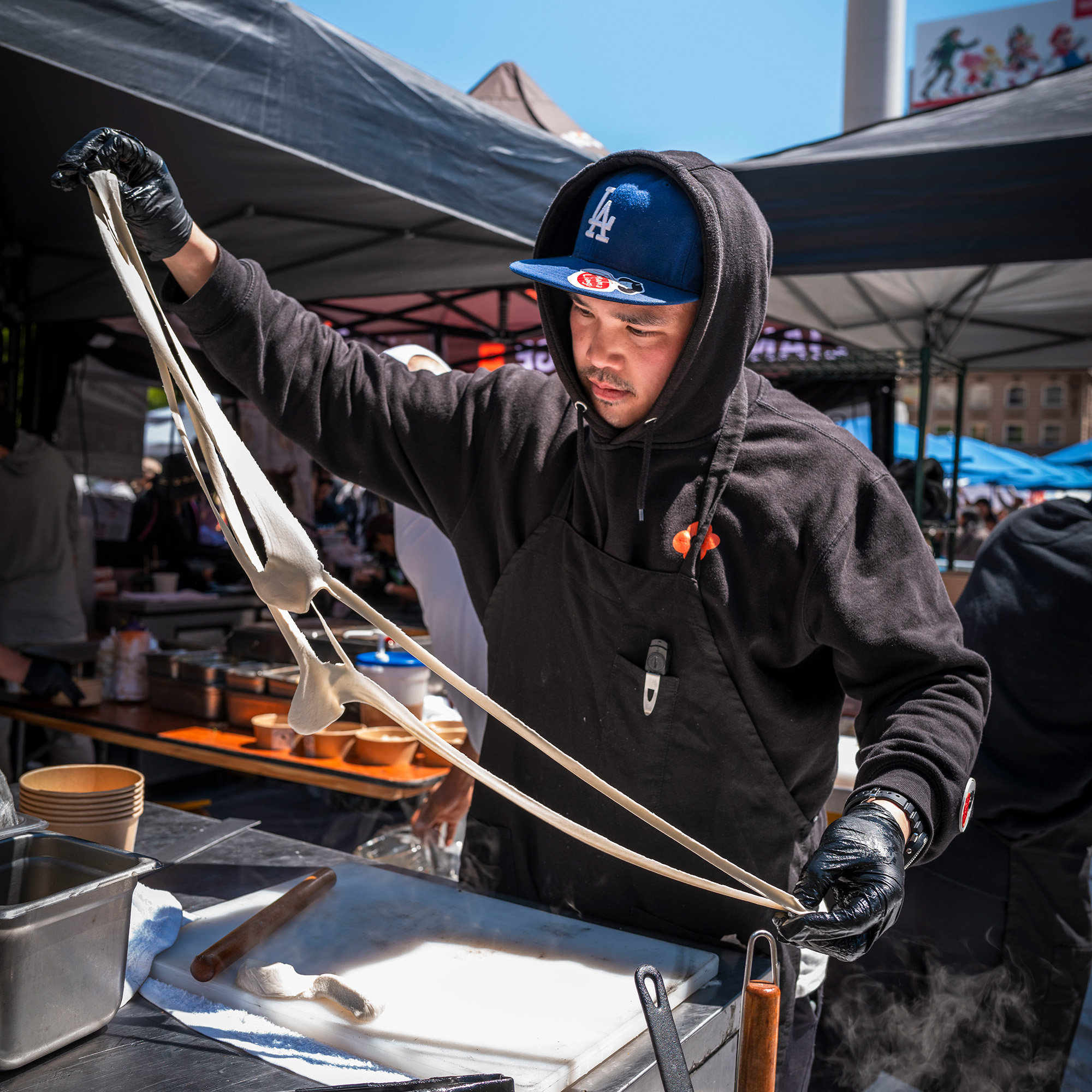 A food vendor pulls noodles at an outdoor festival.