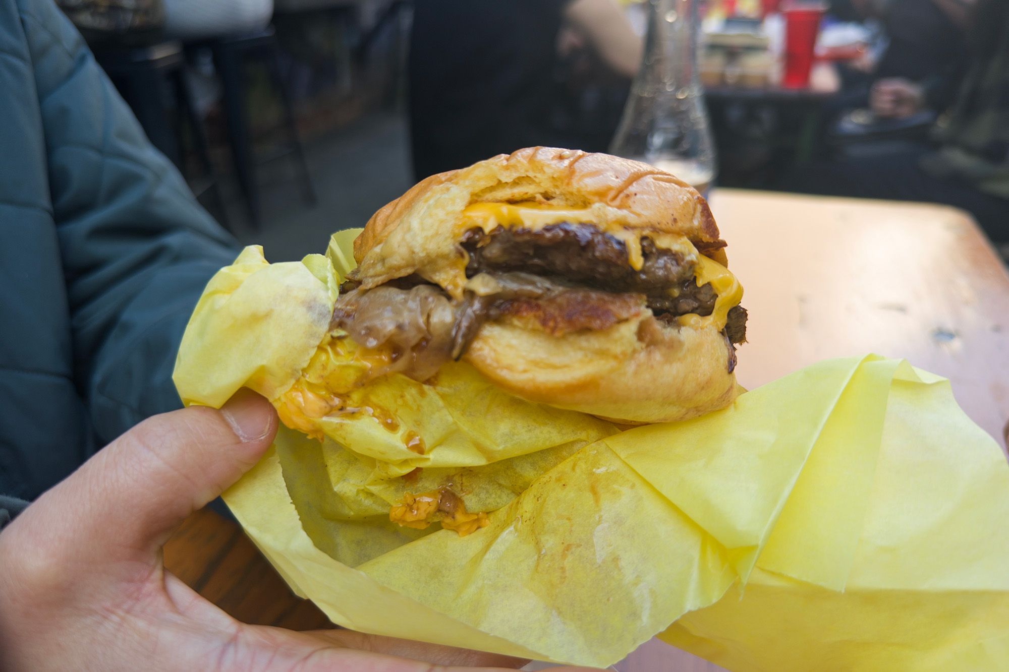 An oozy cheeseburger, just removed from it yellow paper wrapping.