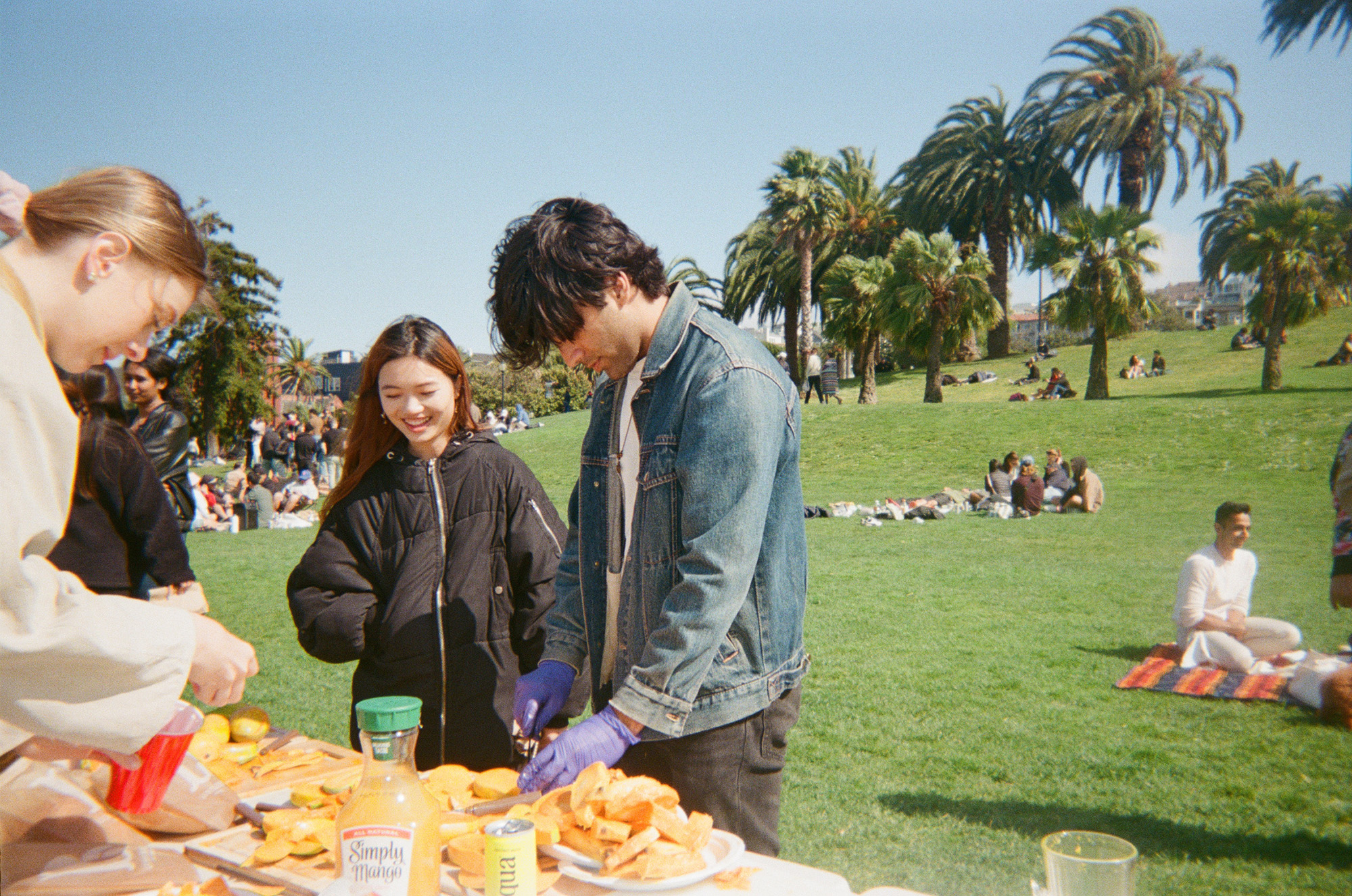 A man slices mangoes outdoors while a smiling woman looks on.
