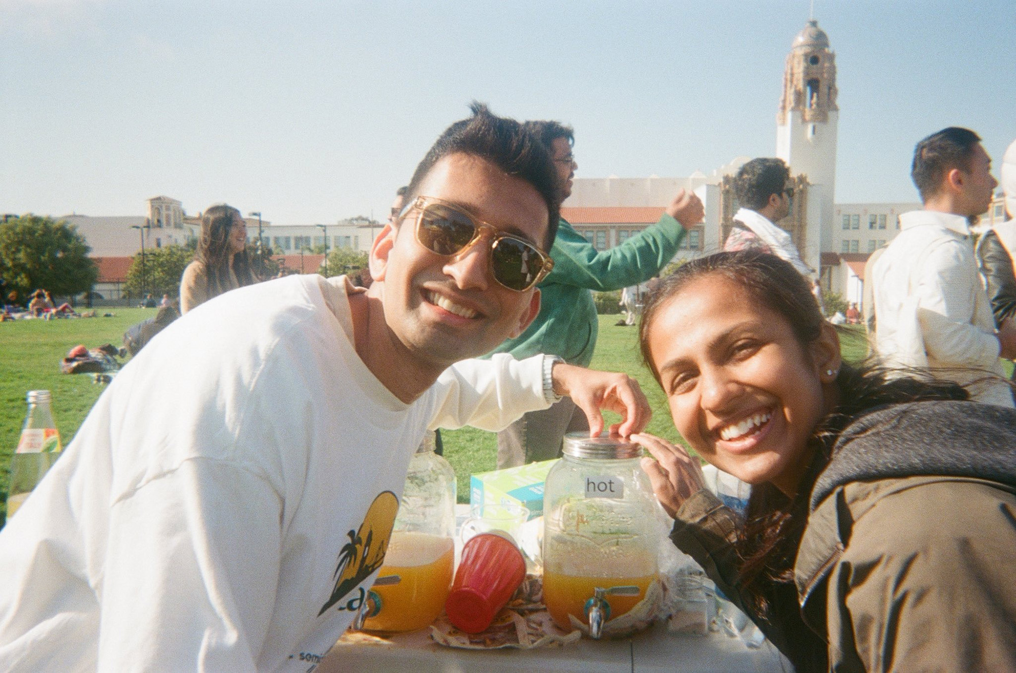 Man and woman pose in front of a mango drink dispenser labeled "hot."