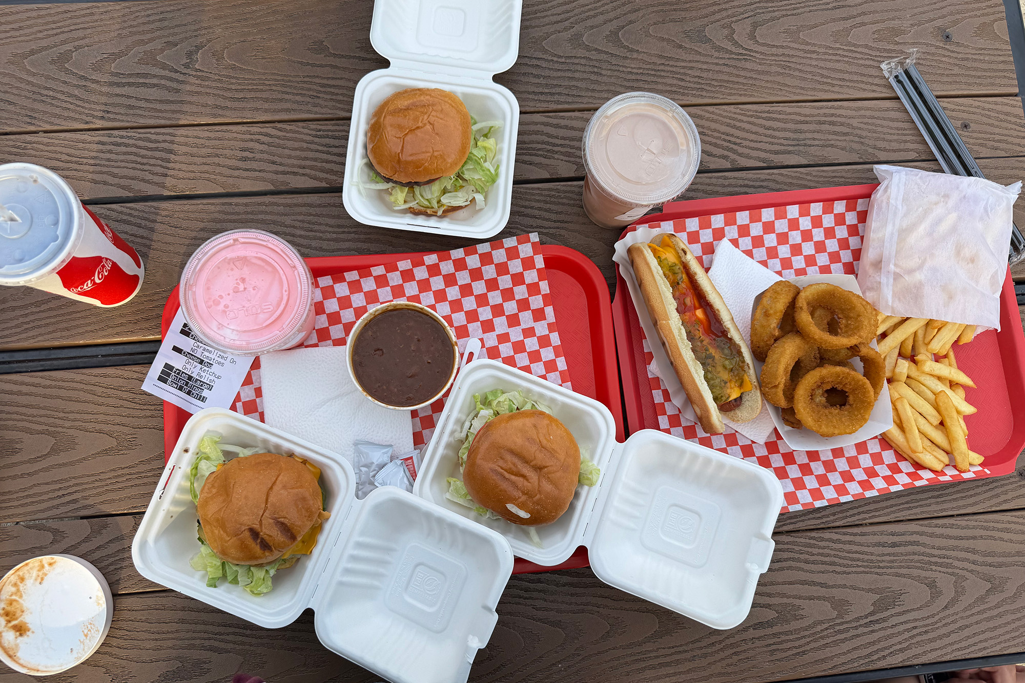 Overhead view of a spread of burgers, fries and milkshakes on a picnic table.