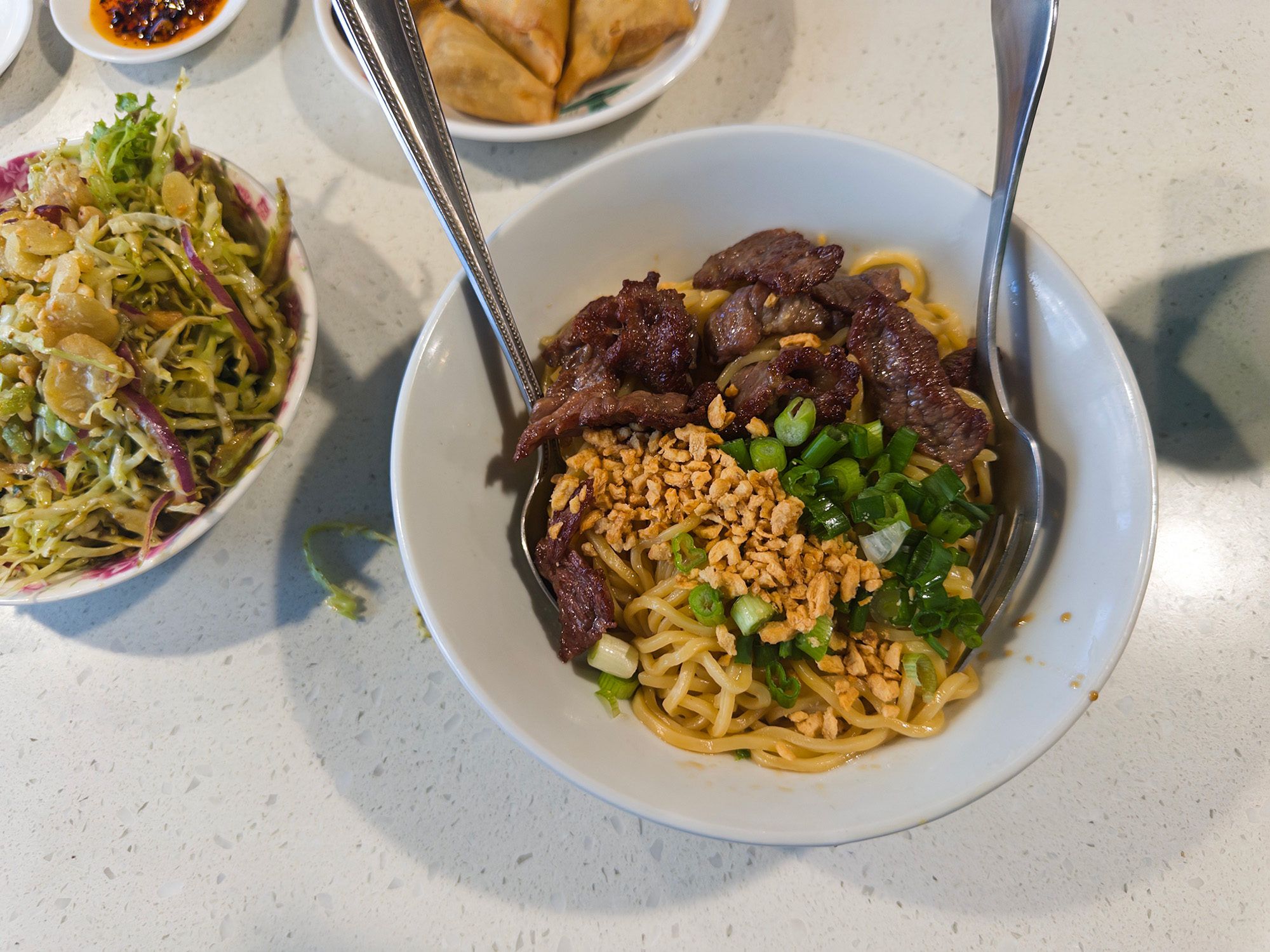 A bowl of beef noodles with Burmese tea leaf salad on the side.
