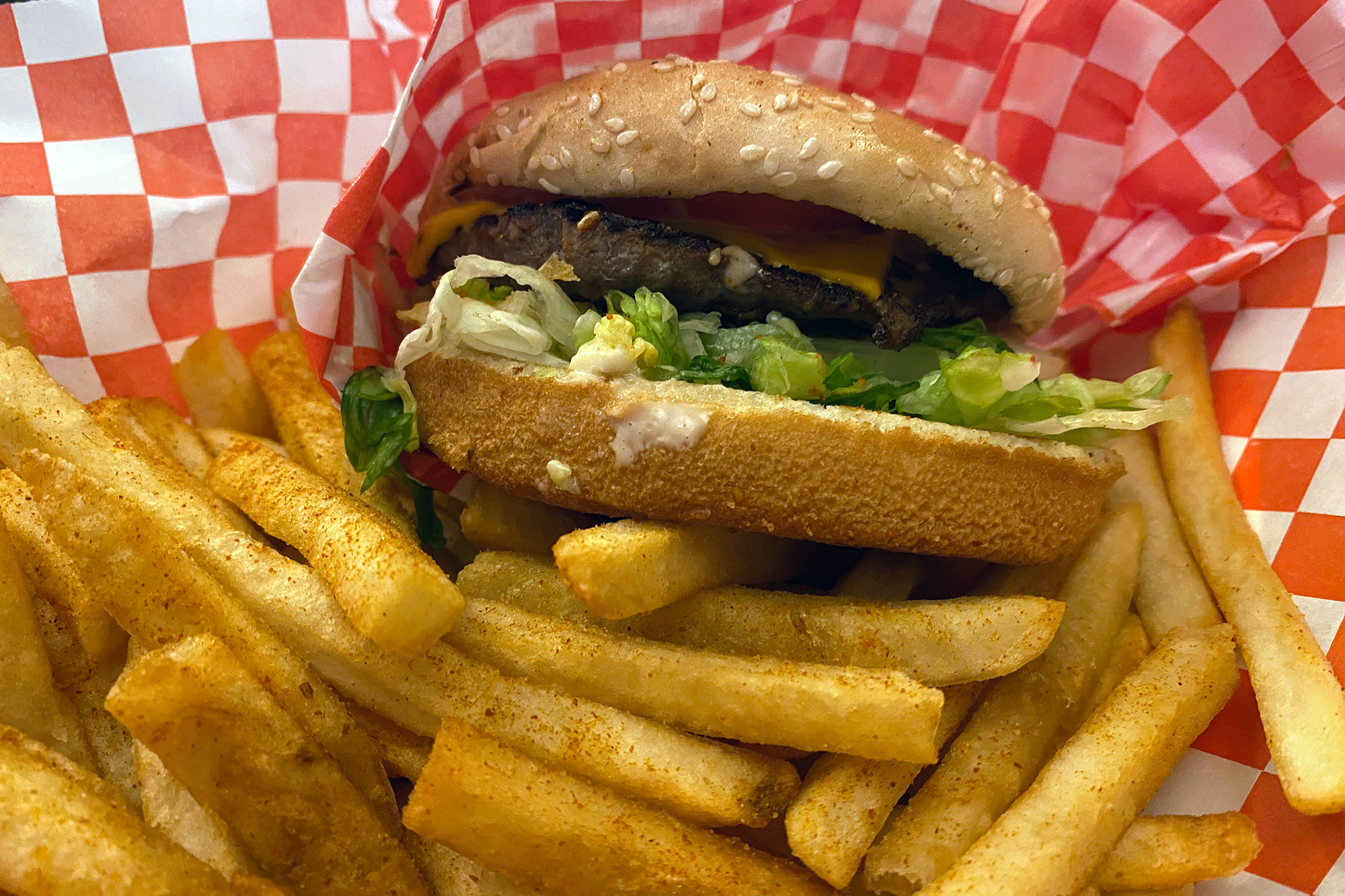 A burger and fries nestled in a red and white checkered paper wrap.