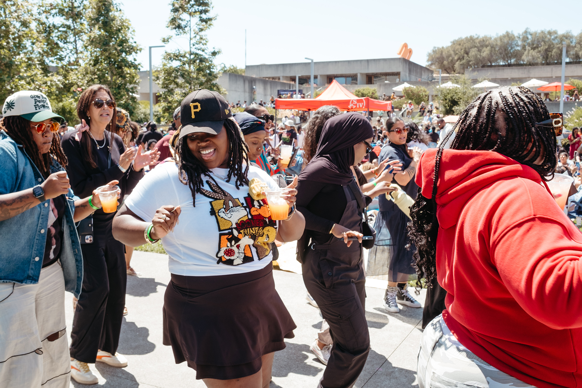 A group of Black women dance as a concrete building and trees stand in the background