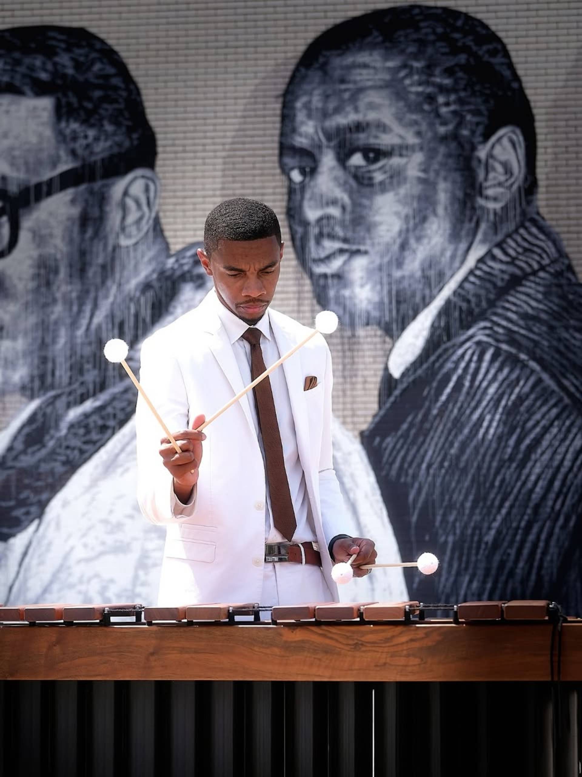 A man in a white suit with a brown tie plays the xylophone.