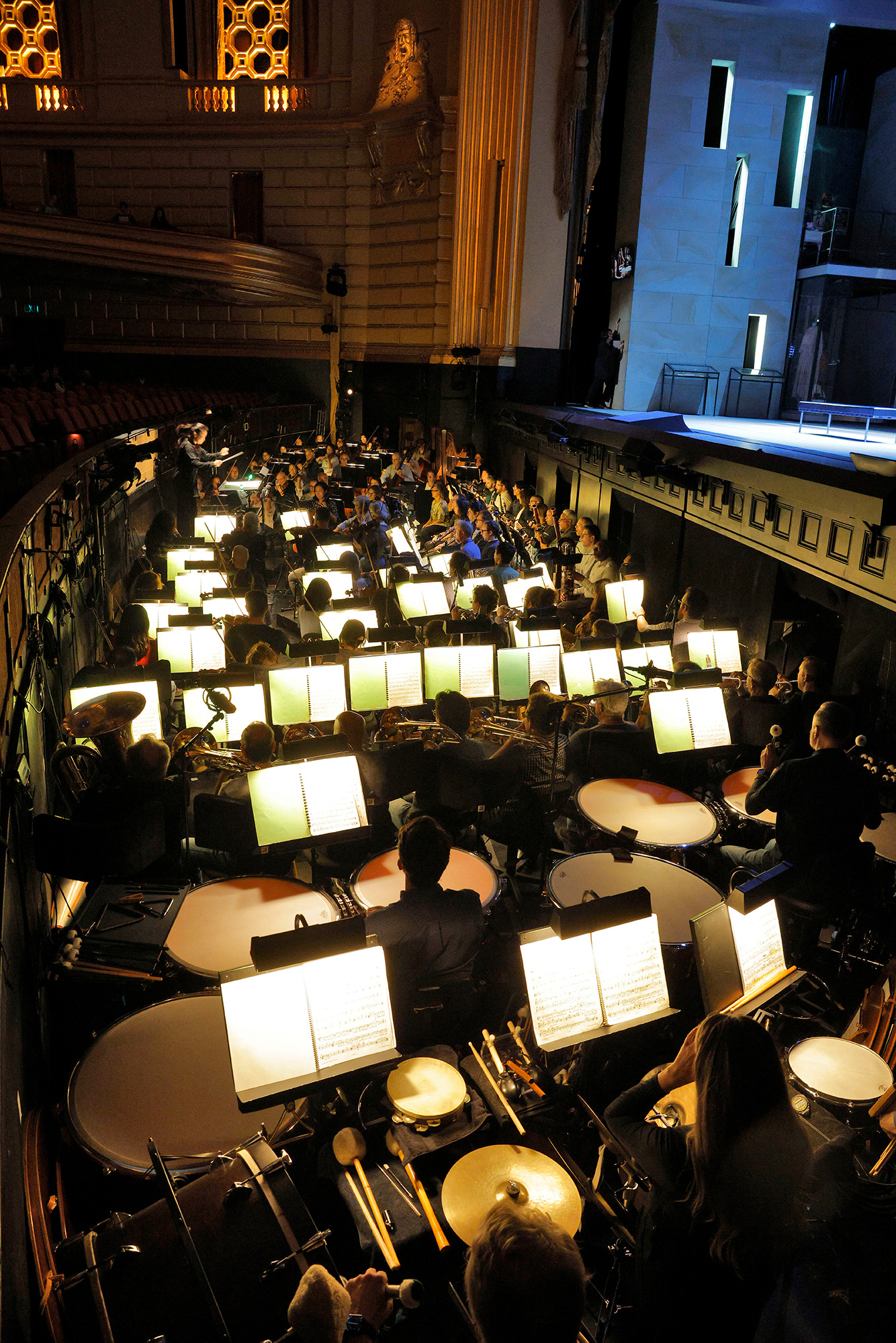 A large orchestra is stuffed tightly into an orchestra pit before a large stage