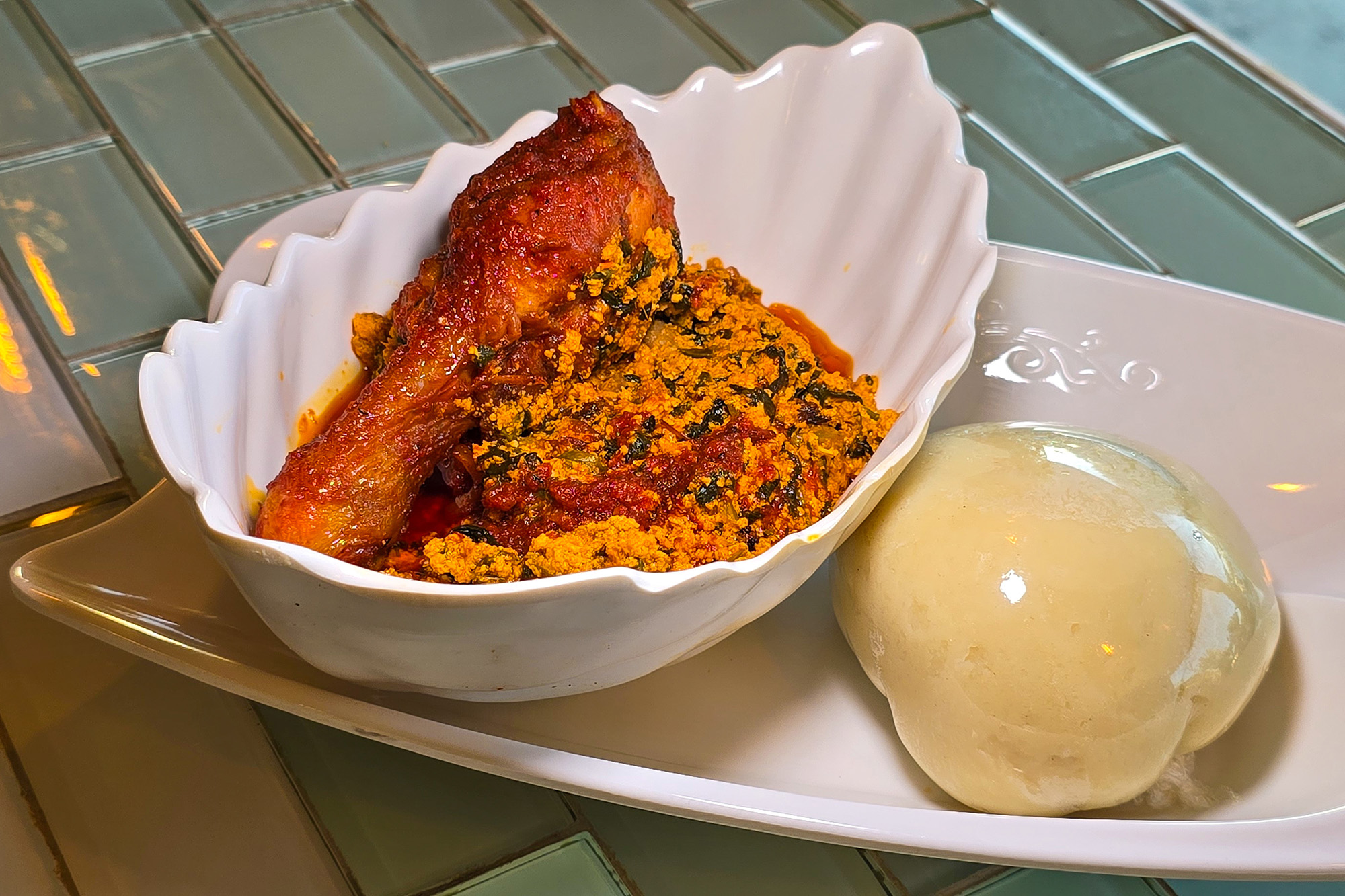 A bowl of egusi soup, served with a white ball of pounded yam on the side.