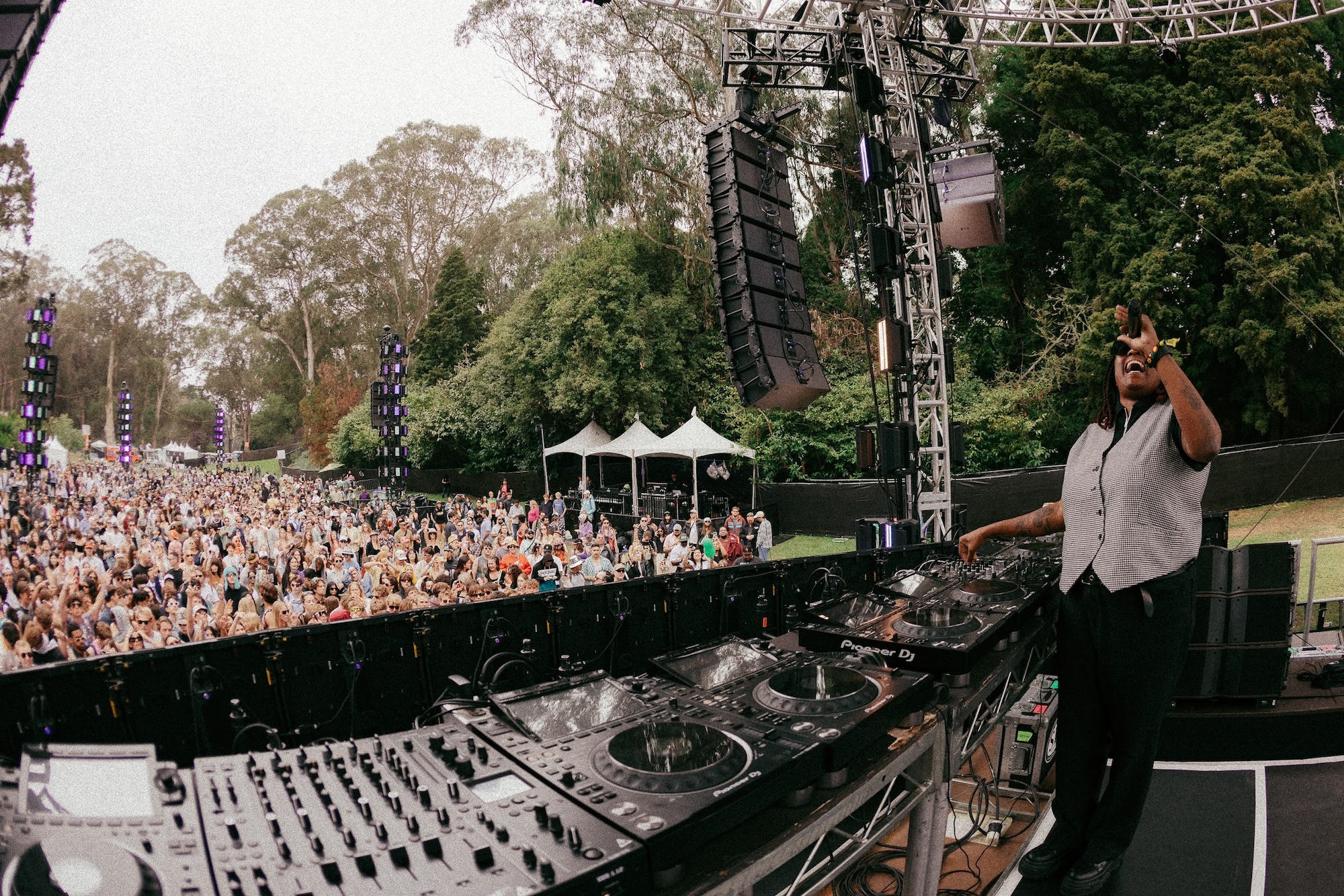 A person standing behind a DJ table at a crowded outdoors event.