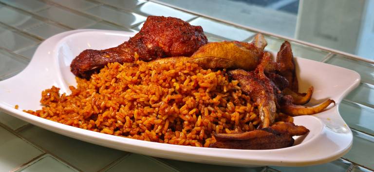 Reddish-orange jollof rice and a chicken leg served on a white plate.