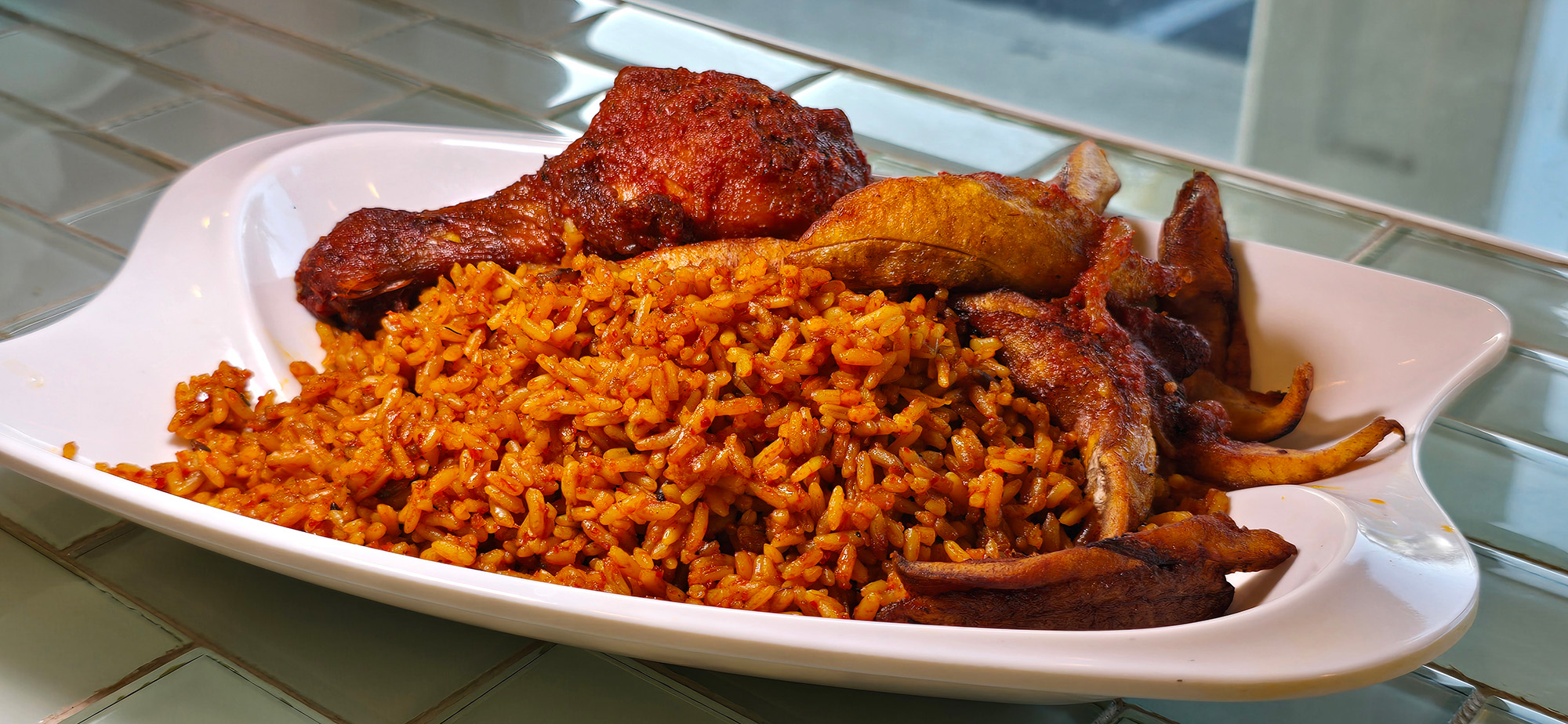 Reddish-orange jollof rice and a chicken leg served on a white plate.