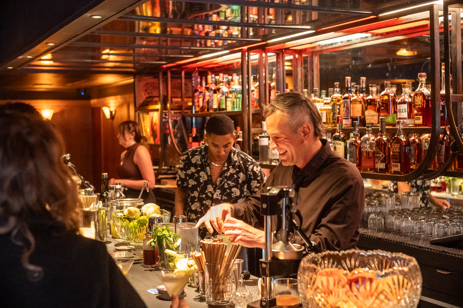 man with shaved sides of head bartends beside coworker in cozy bar