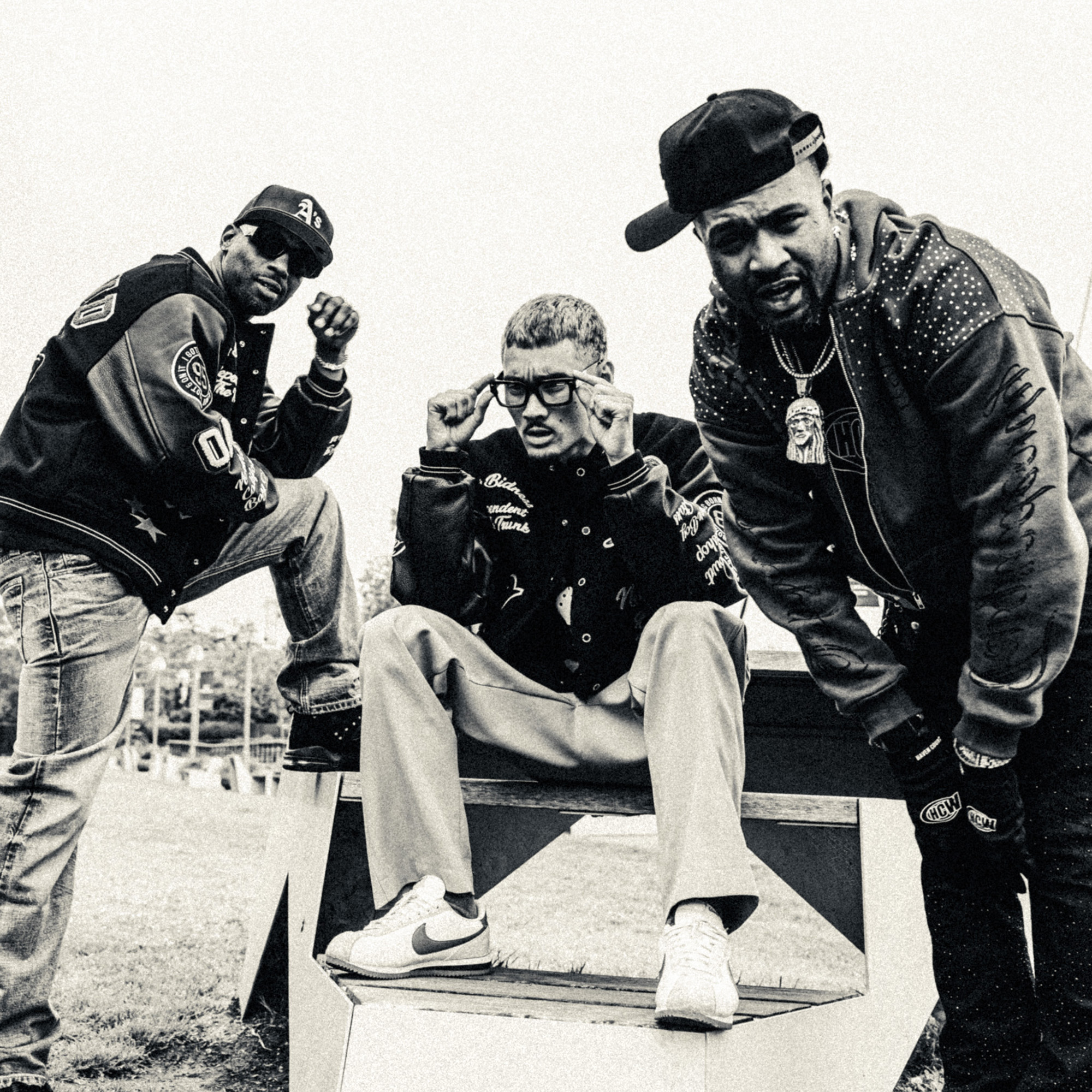 Black and white photo of three rappers in baseball caps mugging for the camera.