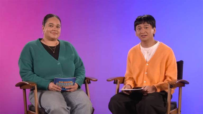 Two twentysomethings sit in folding film-director style chairs against a violet and purple background